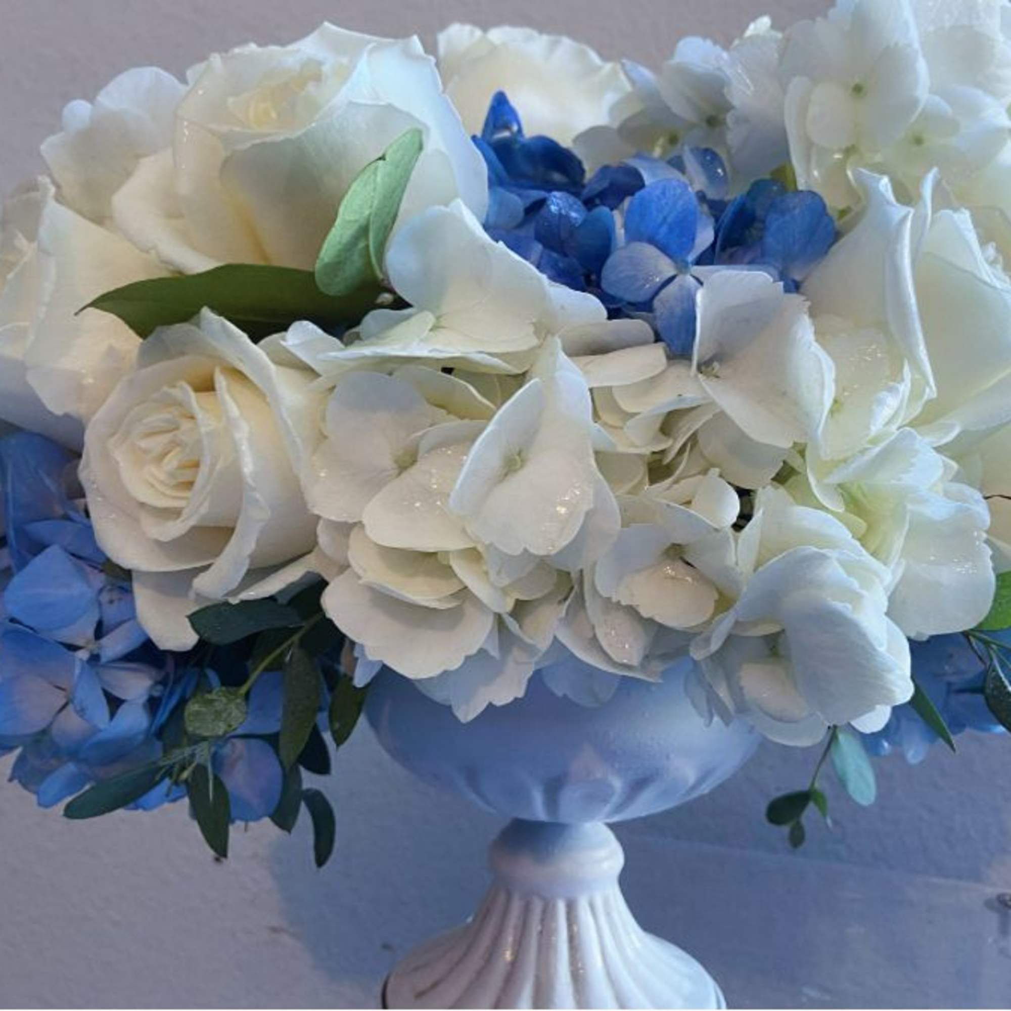 White and blue floral arrangement in a white pedestal vase