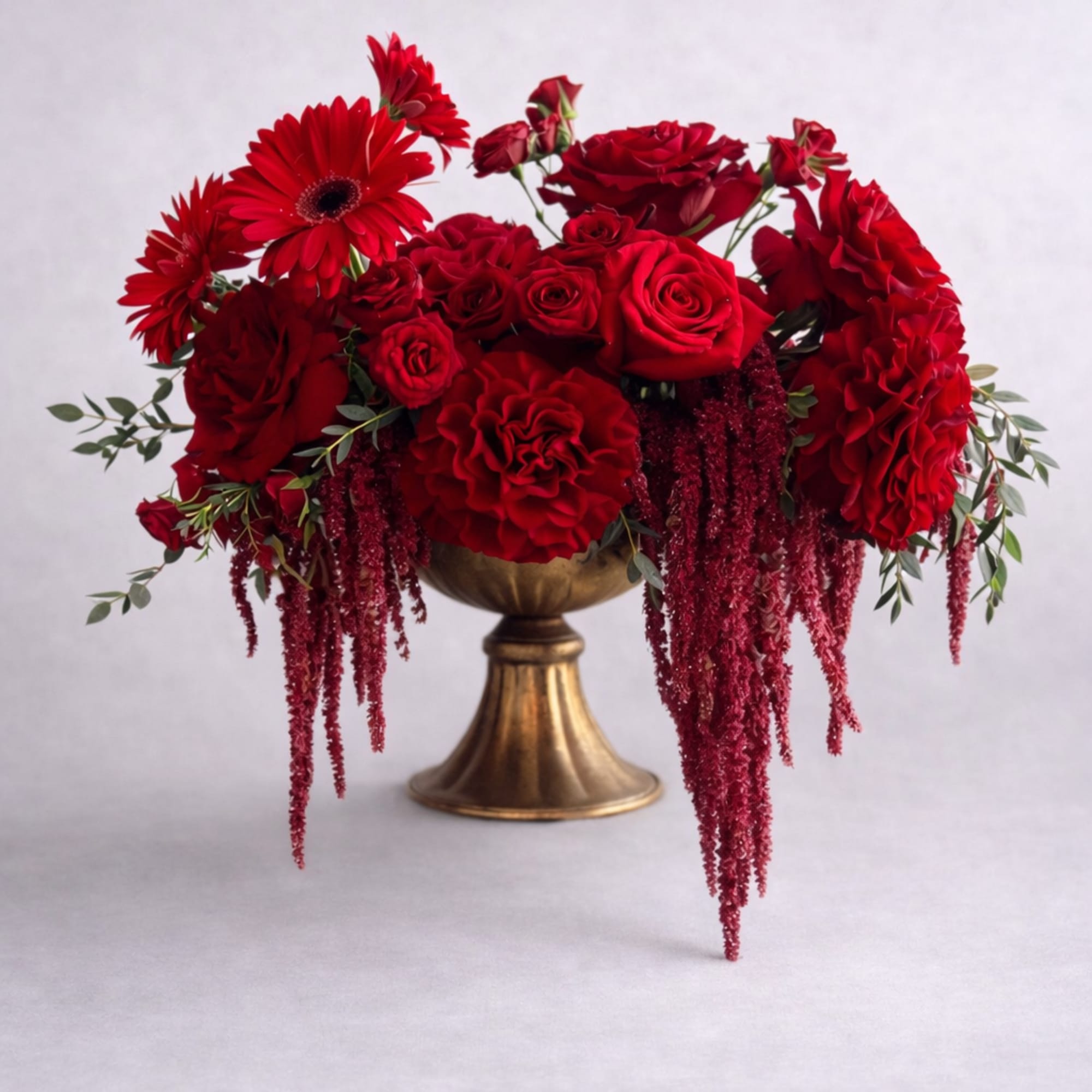 Red roses and gerbera daisies arranged in a gold pedestal vase