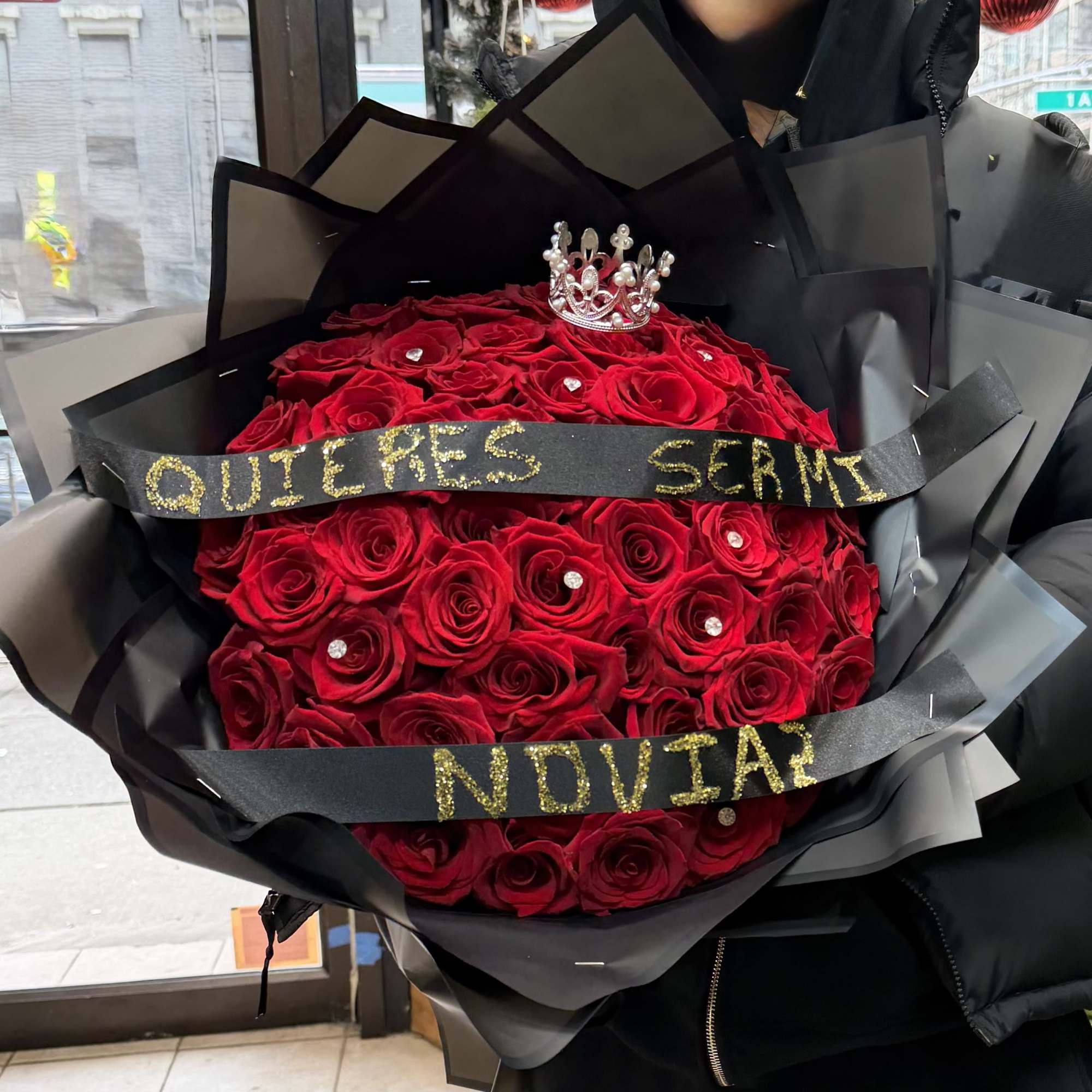 Large bouquet of red roses wrapped in black paper with a small crown