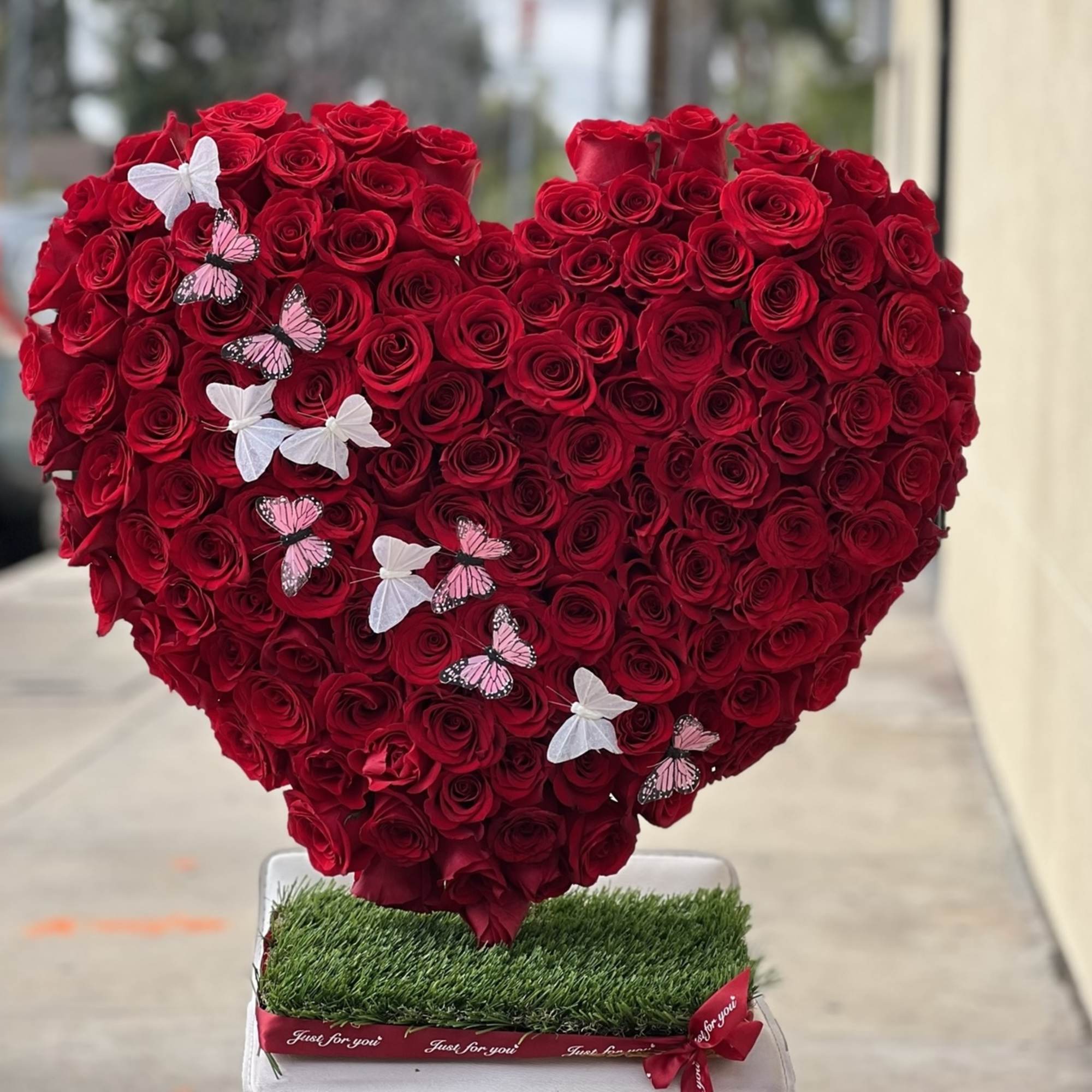 Heart-shaped arrangement of red roses with butterfly decorations on a grass-covered base, photo 2 of 3