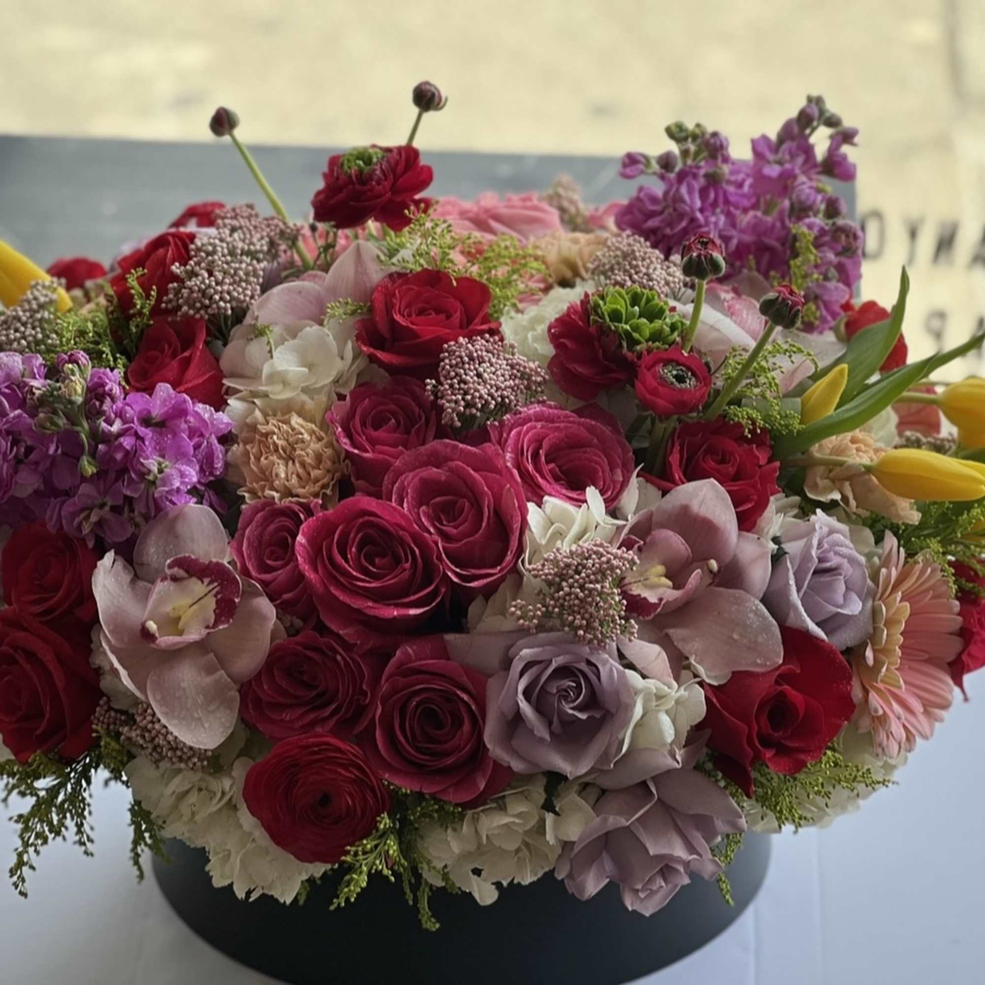 Round bouquet of pink, red, purple, and yellow flowers in a black container