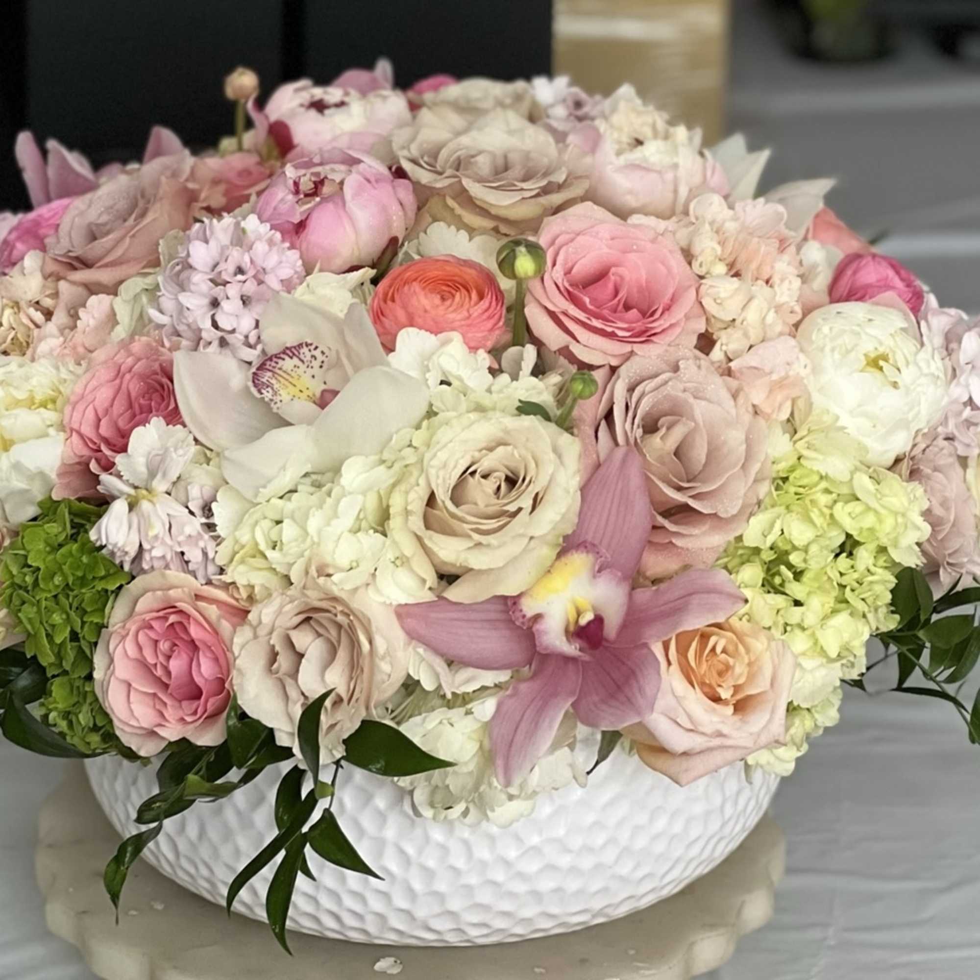 Pink and cream floral arrangement in a white bowl vase