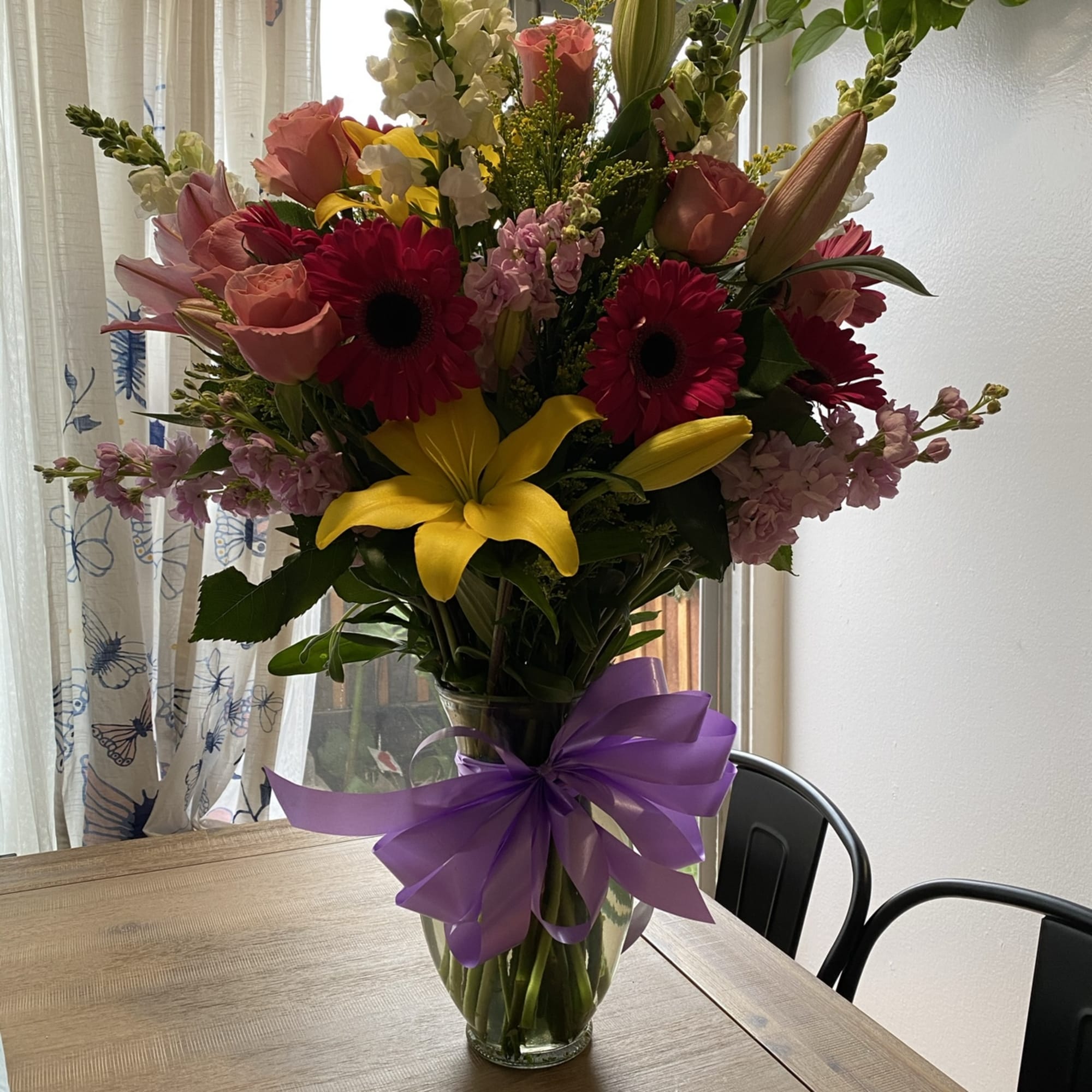 Mixed bouquet of pink, yellow, and white flowers in a glass vase with a purple bow