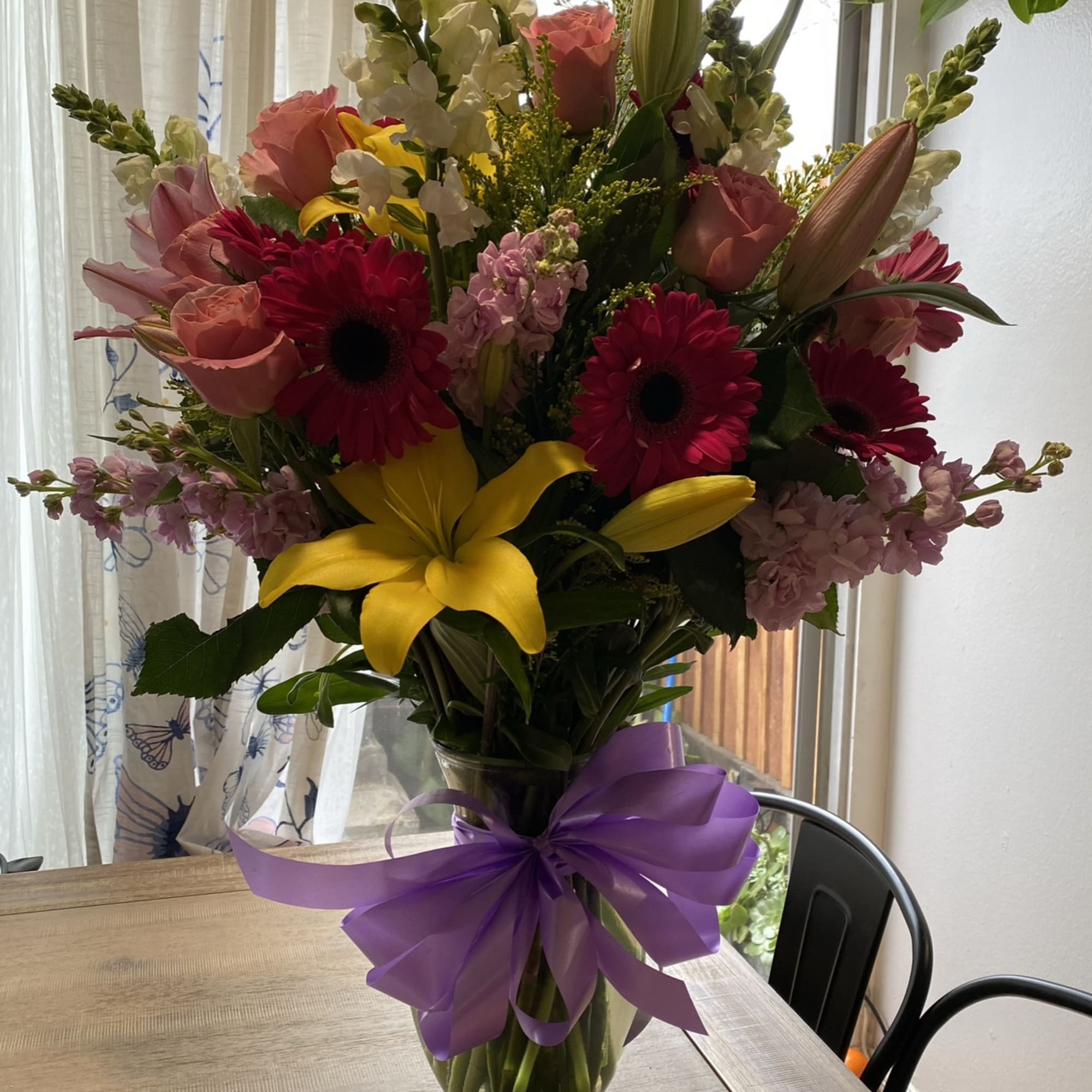 Tall mixed bouquet in a glass vase with a purple ribbon