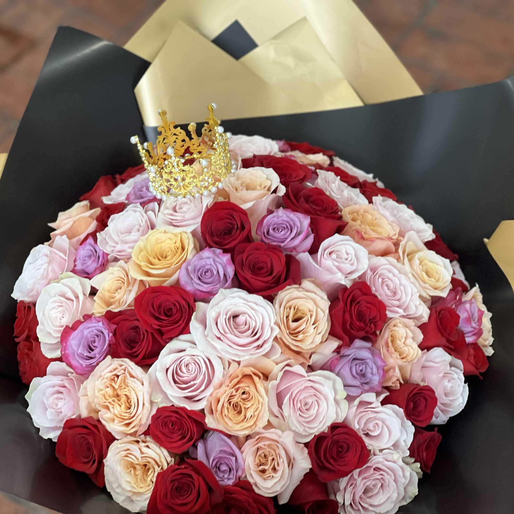 Large bouquet of red, pink, and peach roses with a gold crown topper