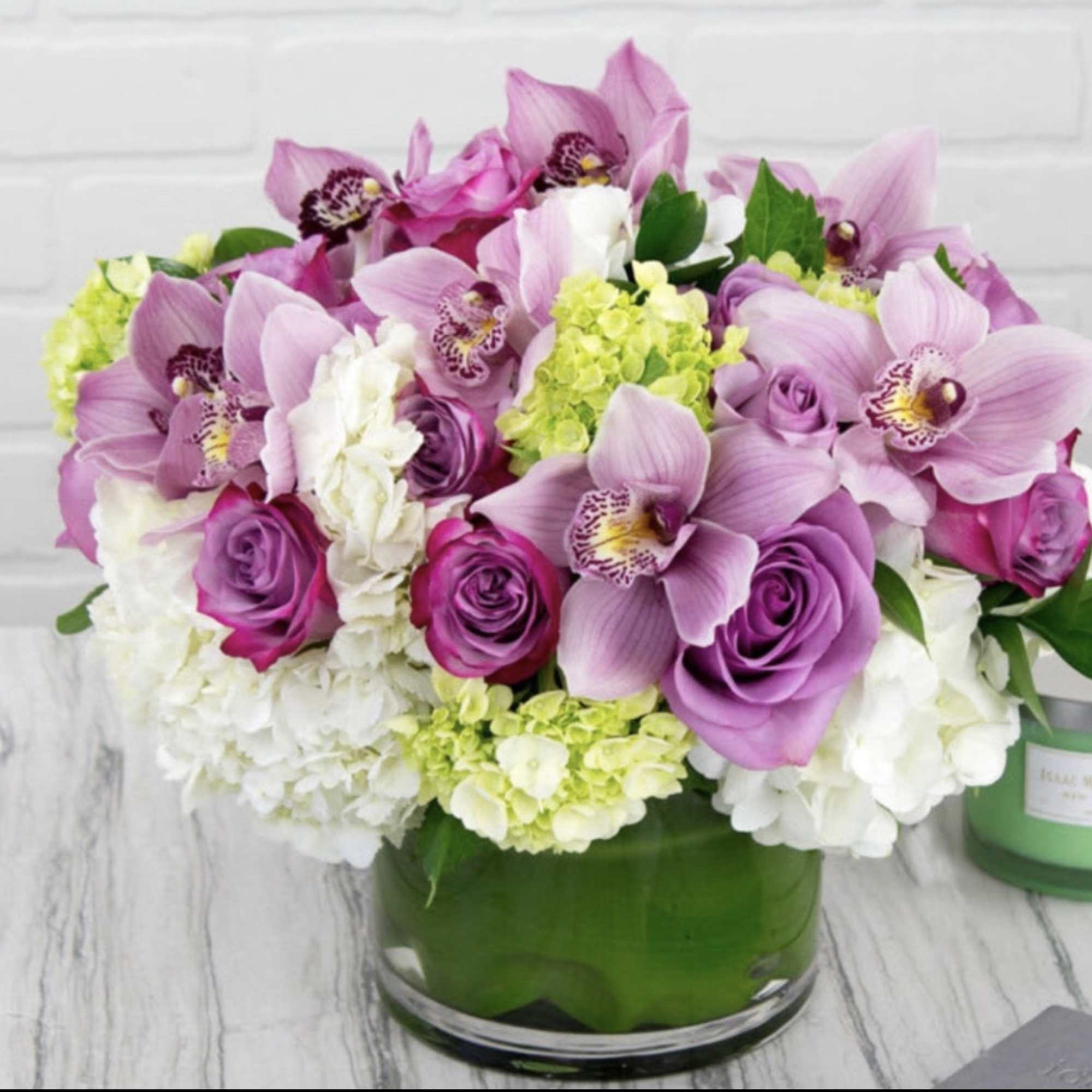 Pink orchids and roses arranged in a green glass vase