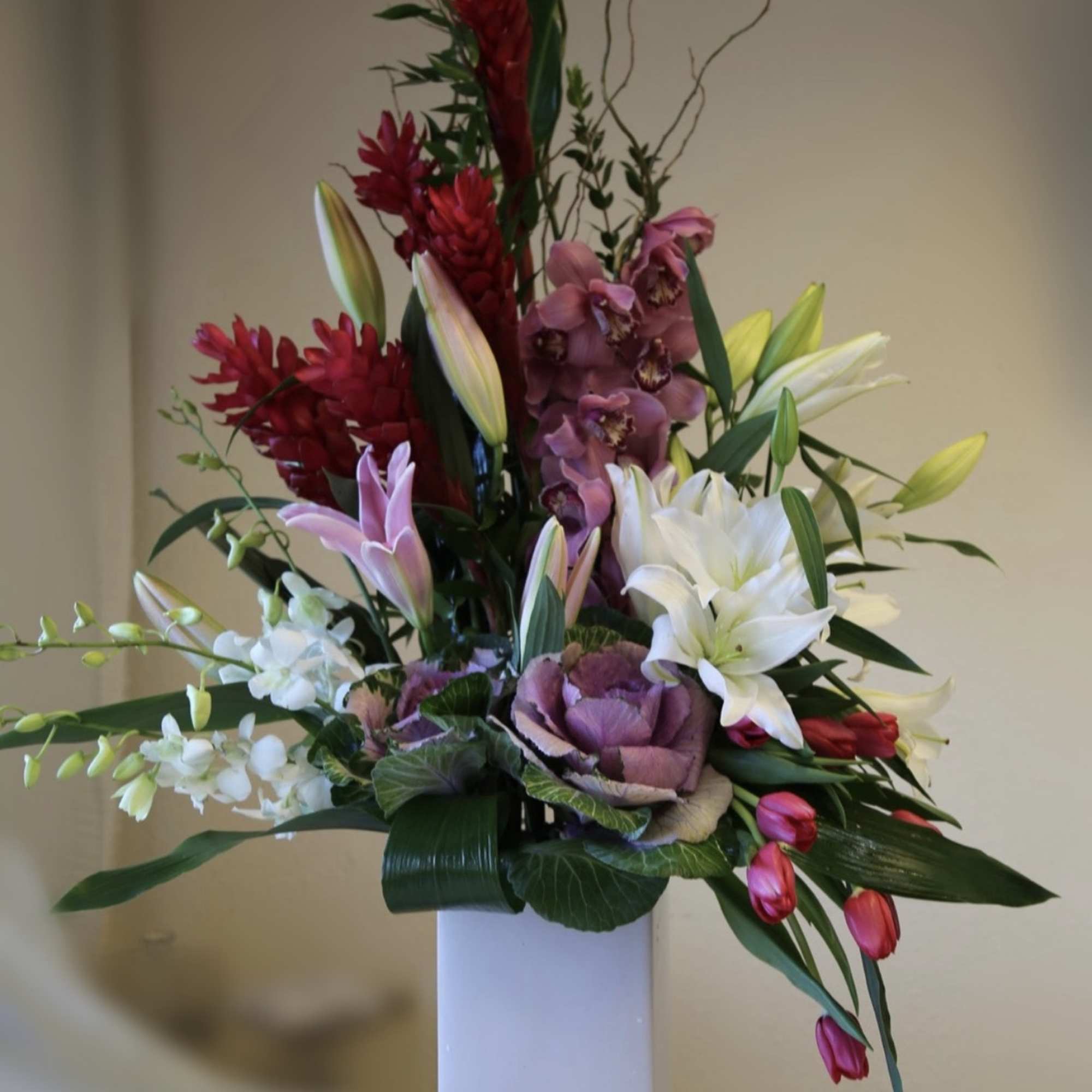 Tall floral arrangement with lilies, orchids, and red tropical blooms in a white vase