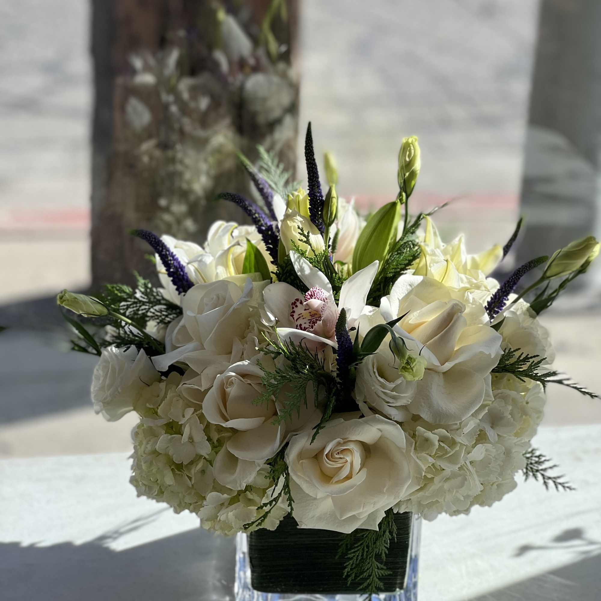 White rose bouquet in a square glass vase with purple spikes