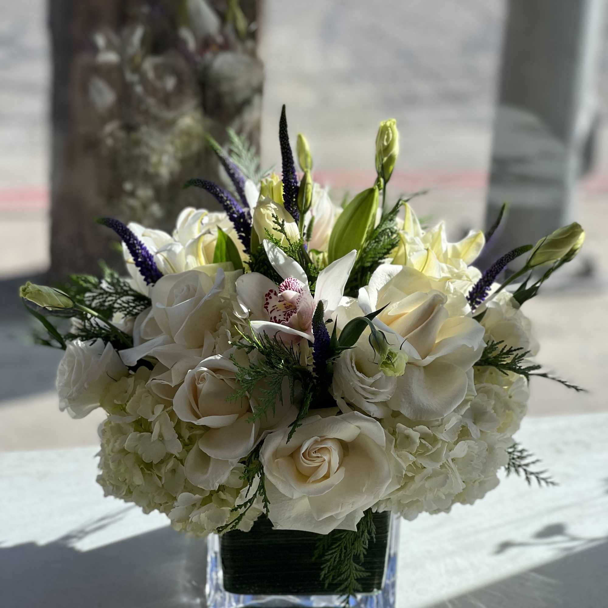 White rose and orchid arrangement in a clear square vase