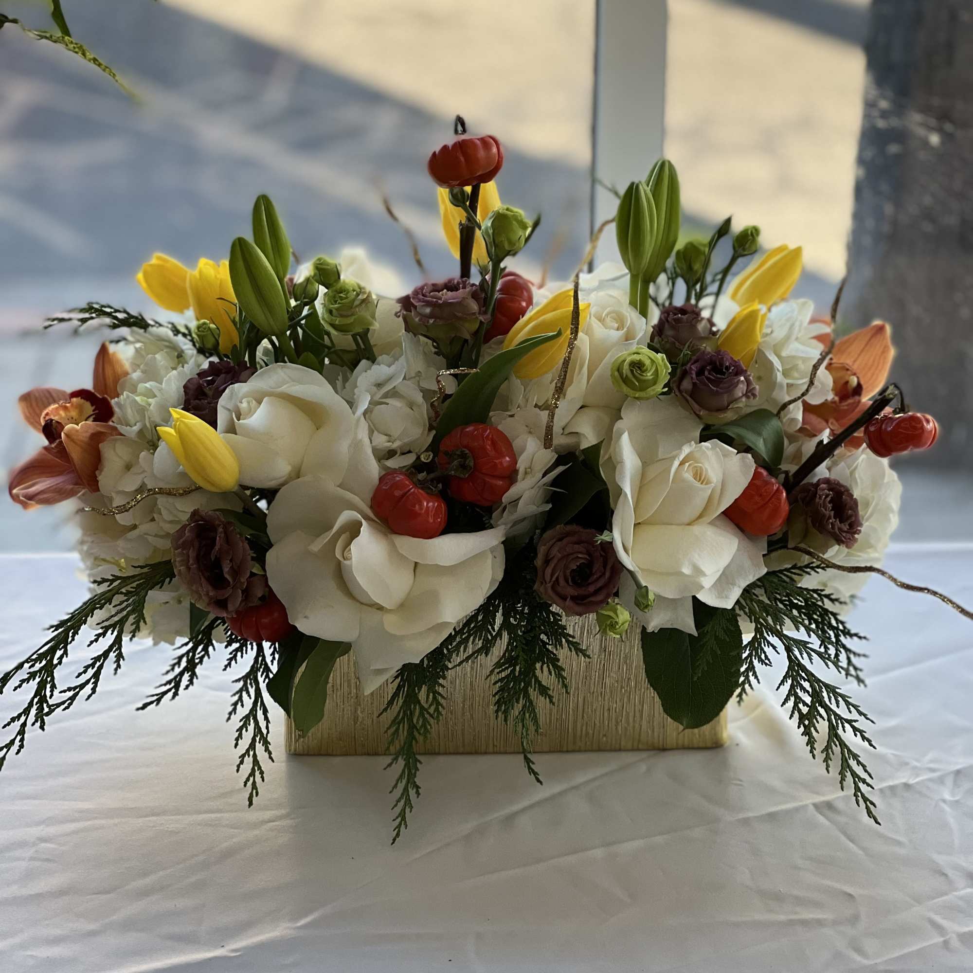 Low floral centerpiece with white roses, yellow tulips, and red berries in a wooden box