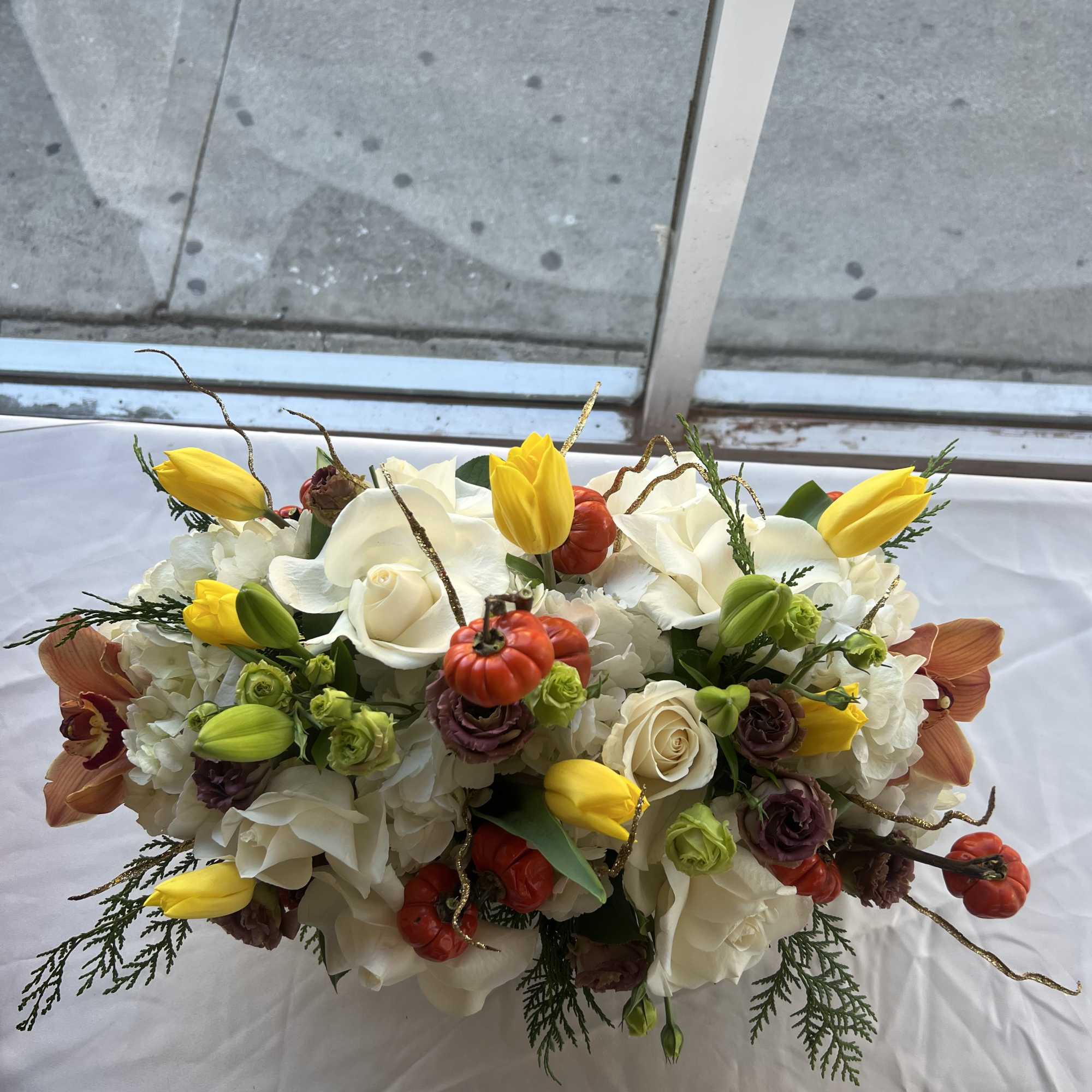 White floral arrangement with yellow tulips and small orange pumpkins