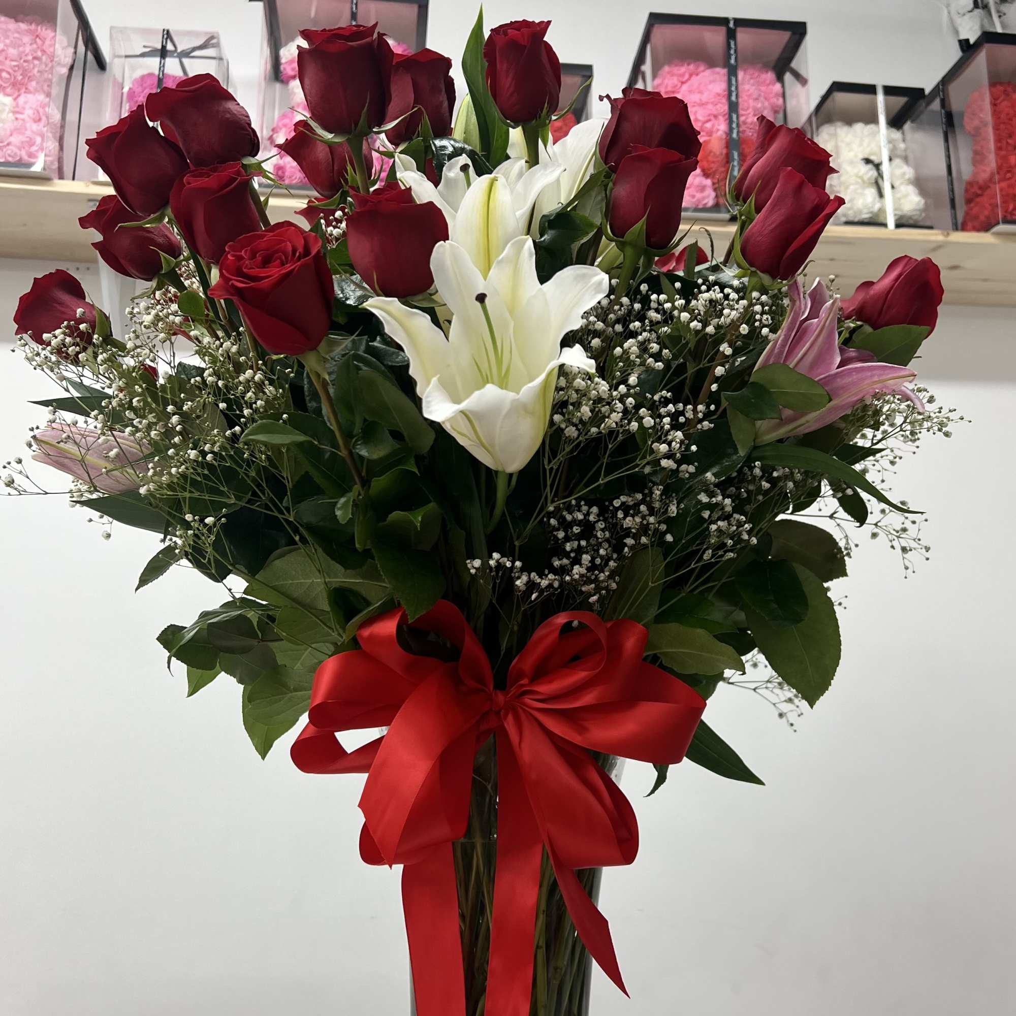Tall bouquet of red roses and white lilies in a glass vase with a red ribbon