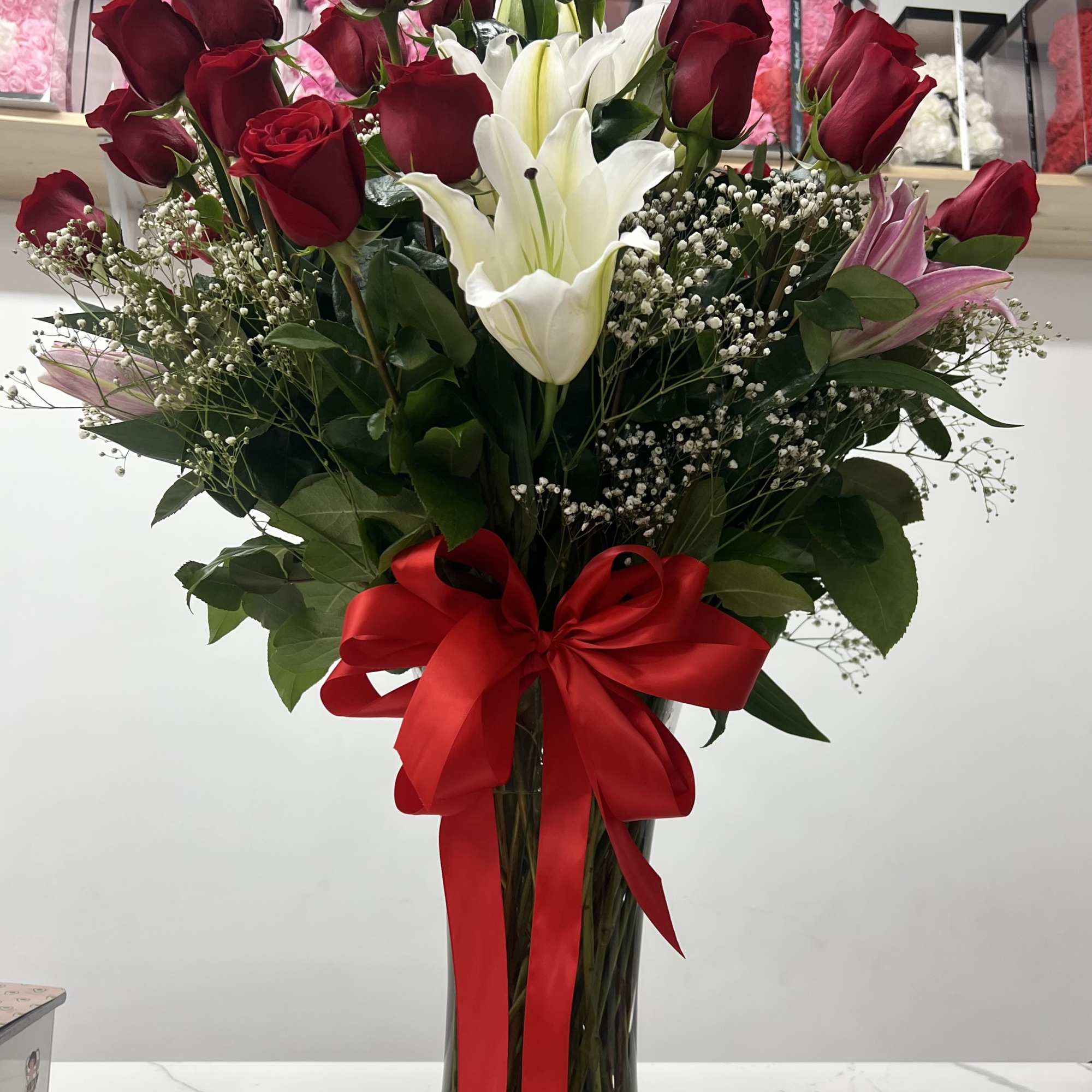 Tall bouquet of red roses and white lilies in a glass vase with a red ribbon.