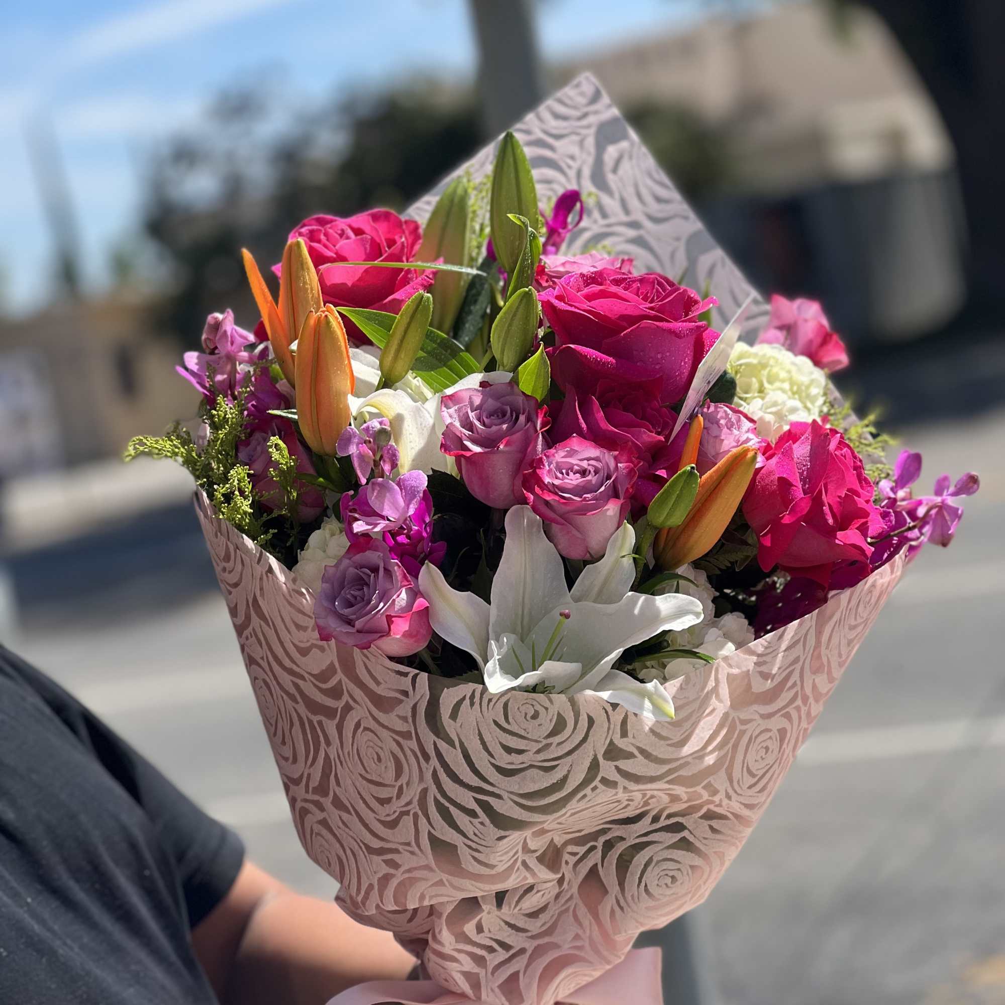 Bouquet of pink roses, lilies, and purple flowers wrapped in patterned paper