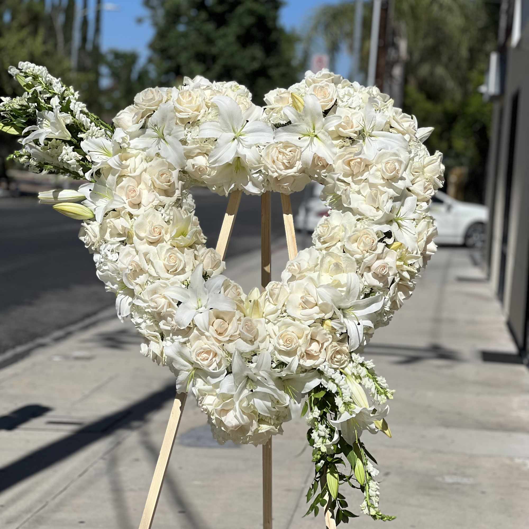 Heart-shaped white floral wreath on a wooden stand
