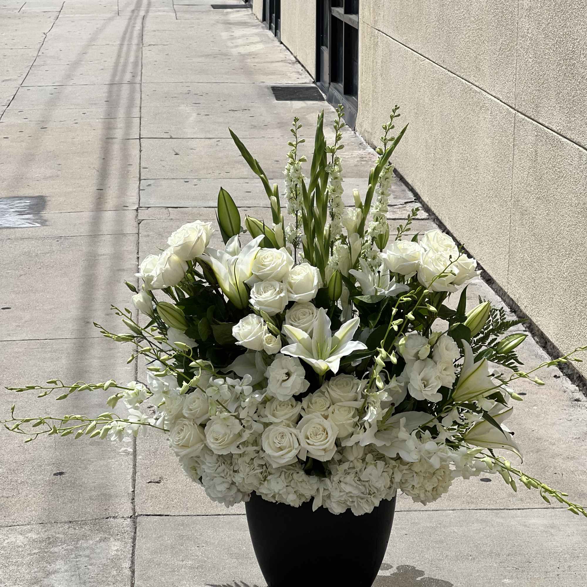 Large white floral arrangement in a black vase on a sidewalk