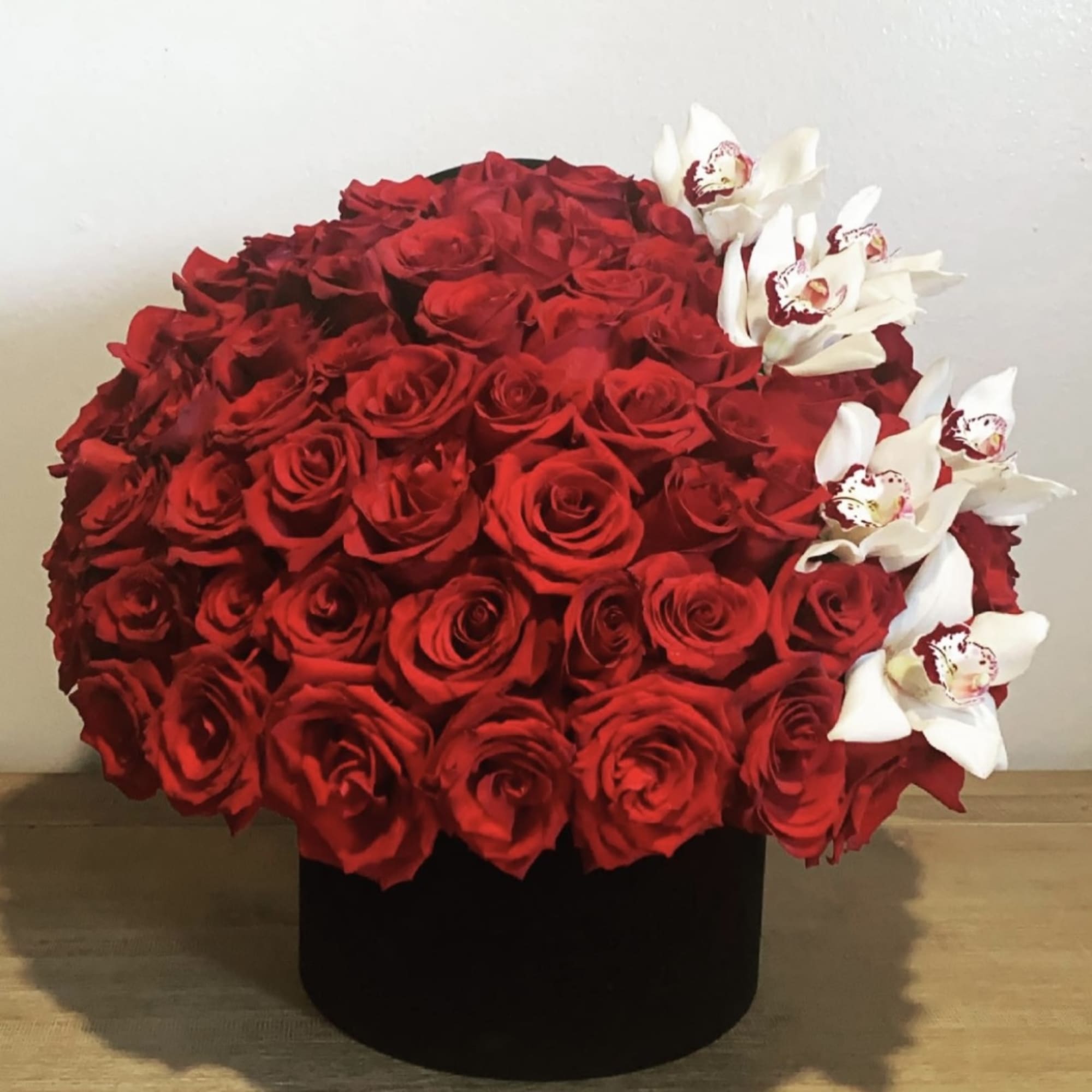 Large red rose arrangement with white orchids in a black box