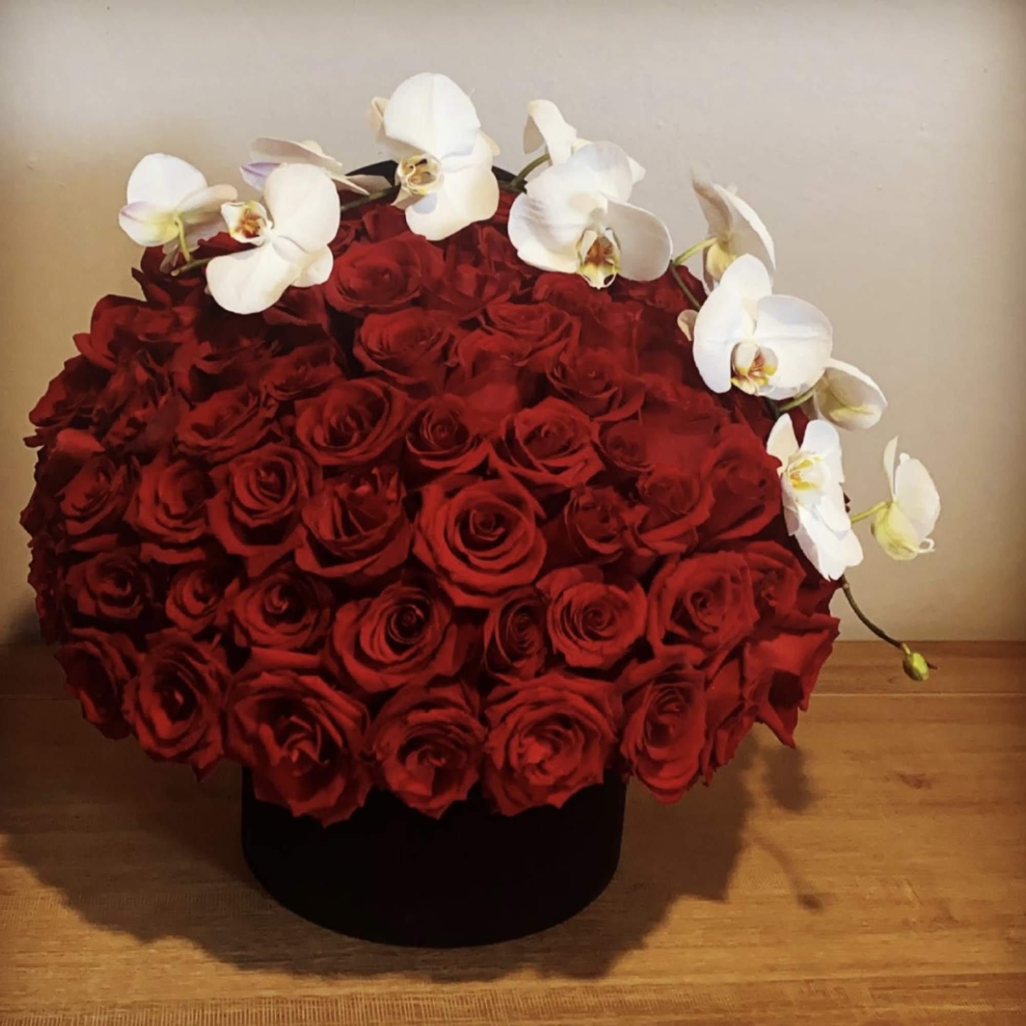 Round arrangement of red roses topped with white orchids in a black box