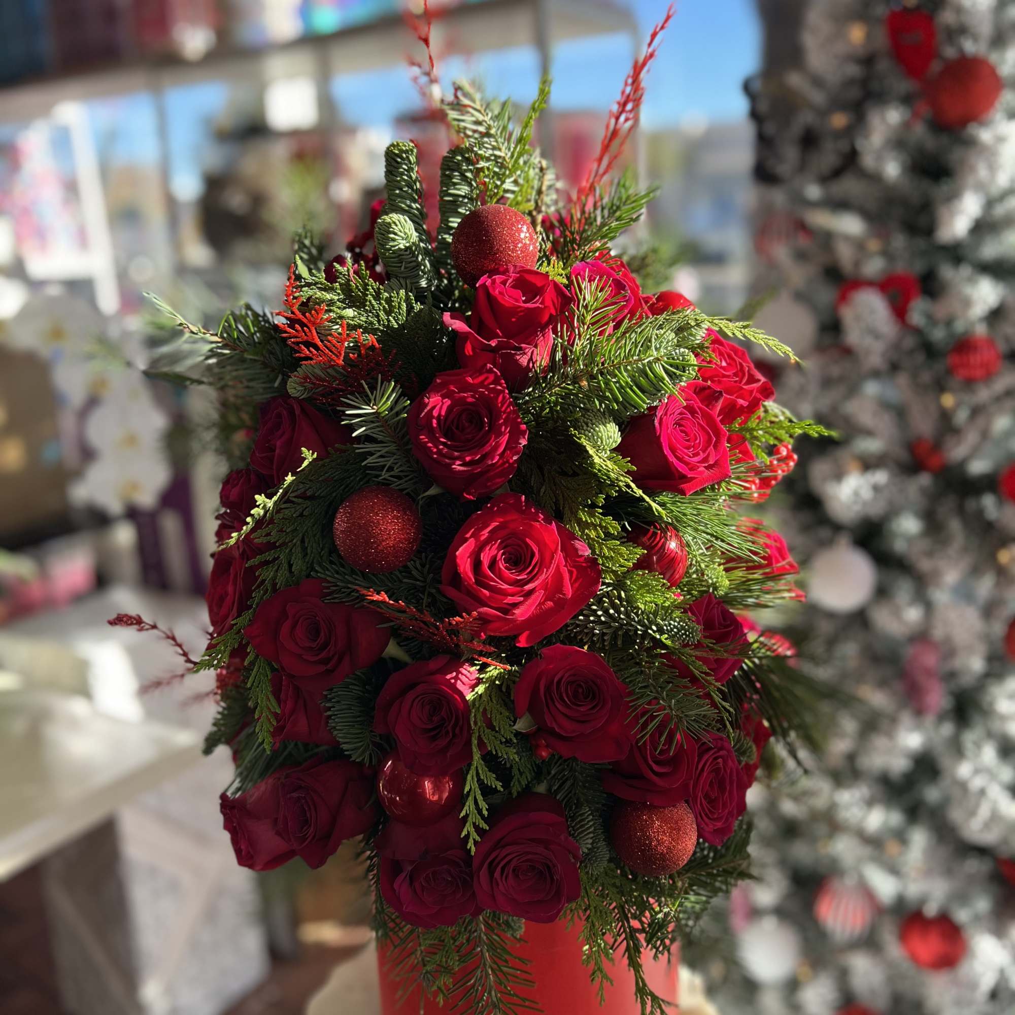 Red roses arranged with evergreen and red ornaments in a red container