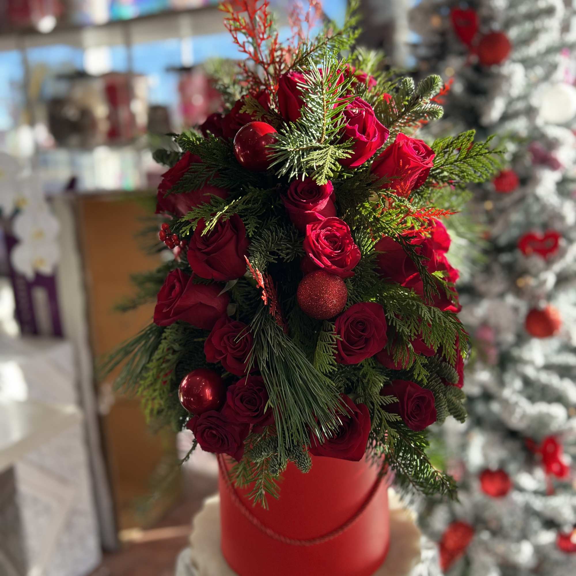 Red roses arranged with evergreen branches in a red hatbox