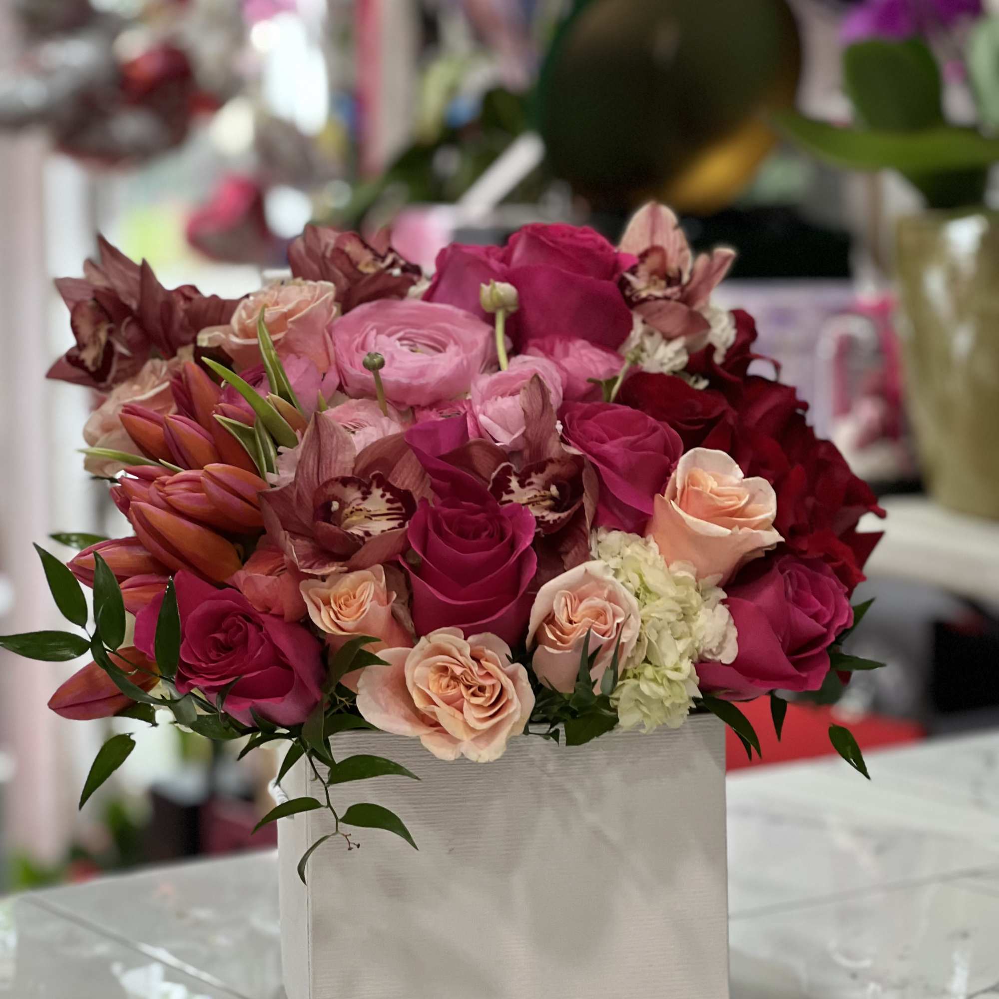 Pink and red roses arranged in a white square box