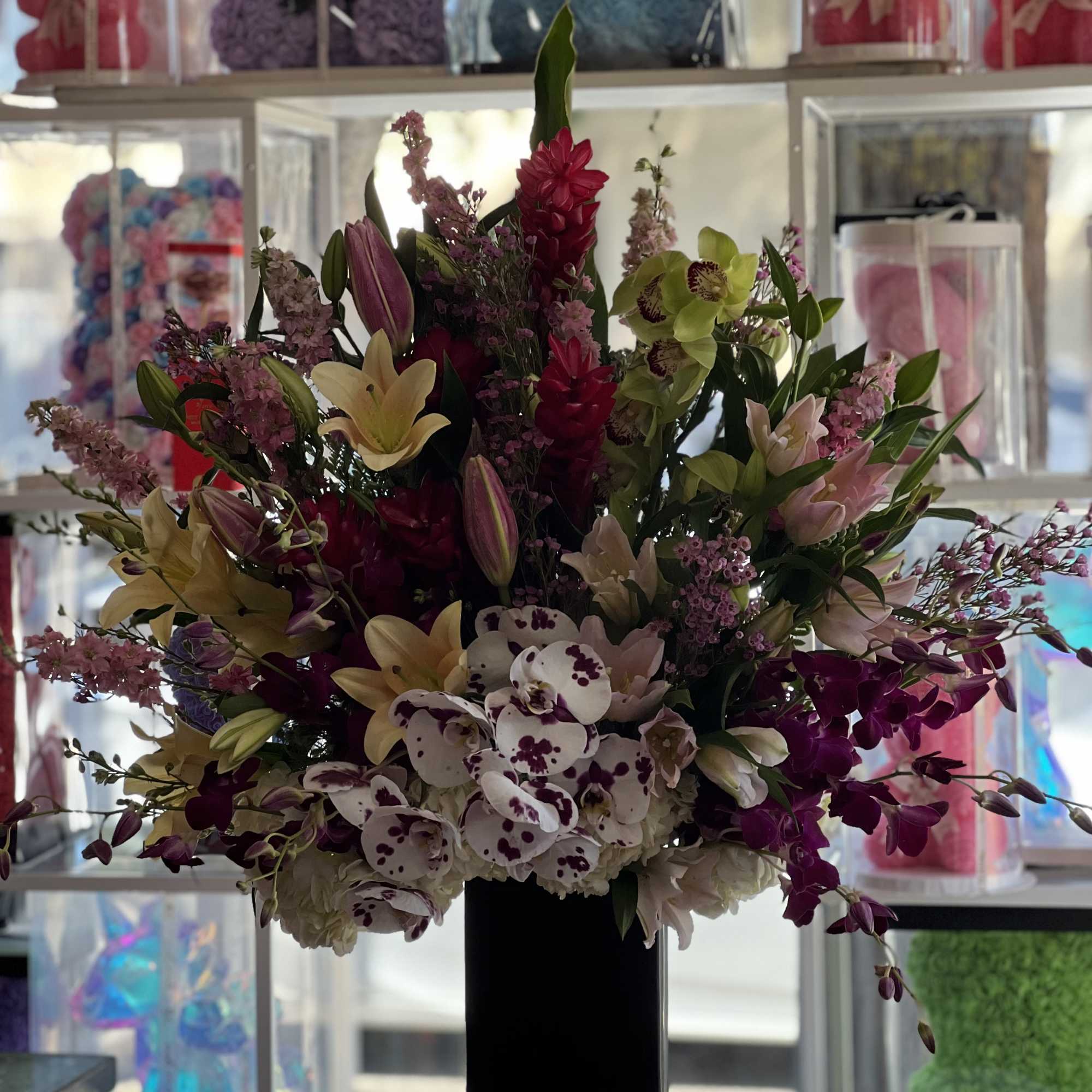 Tall floral arrangement with orchids, lilies, and hydrangeas in a black vase
