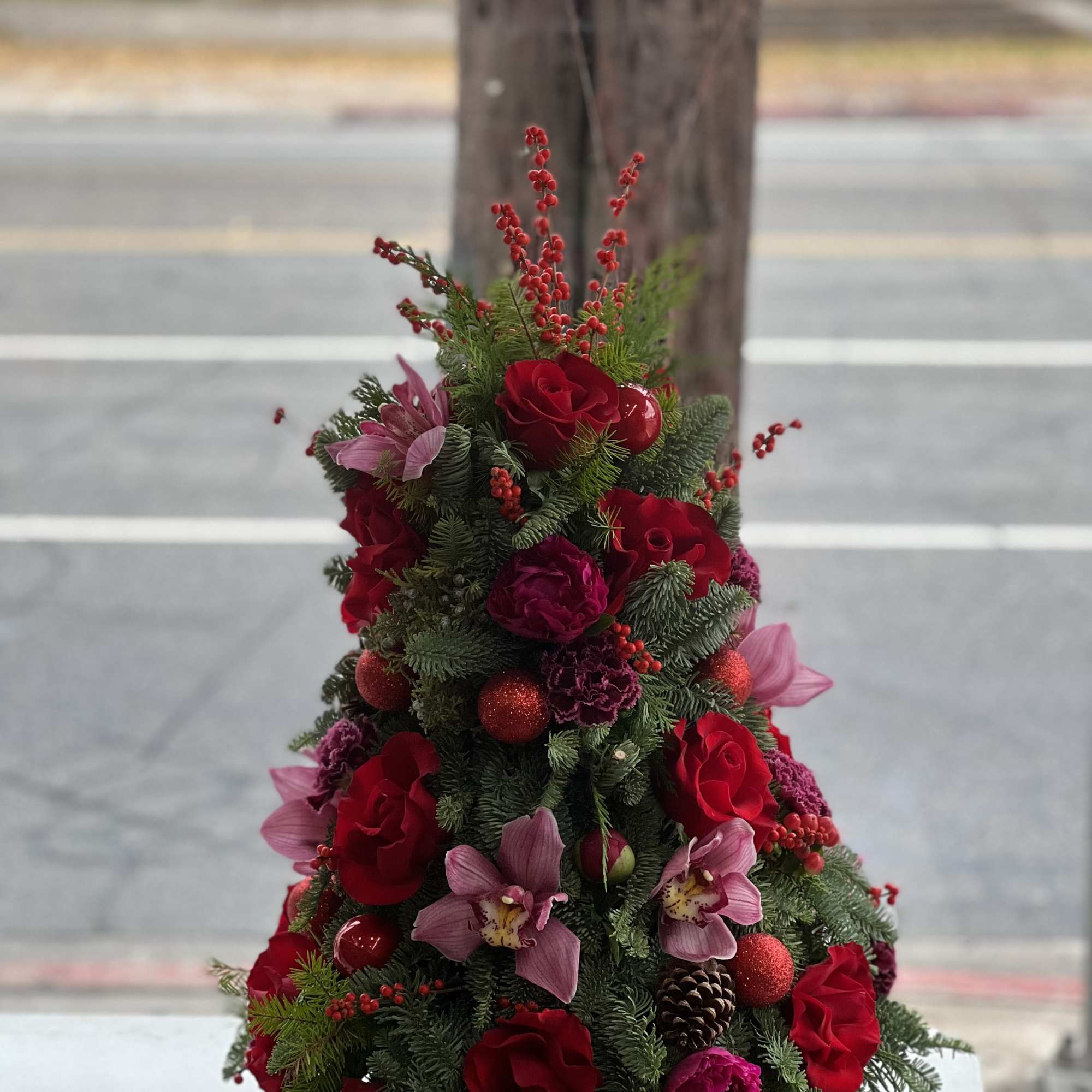 Christmas tree-shaped floral arrangement with red roses and pink orchids in a white pot