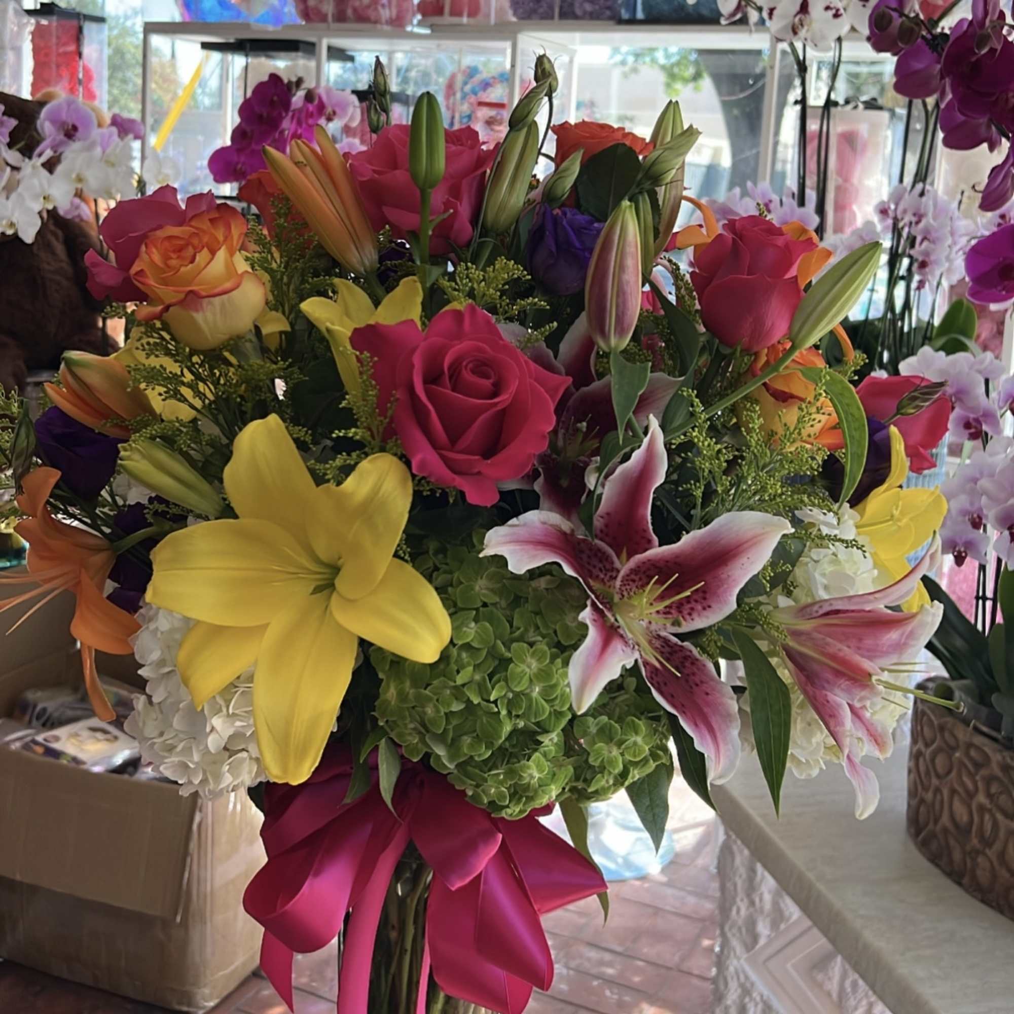 Colorful bouquet of roses and lilies with a pink ribbon in a glass vase