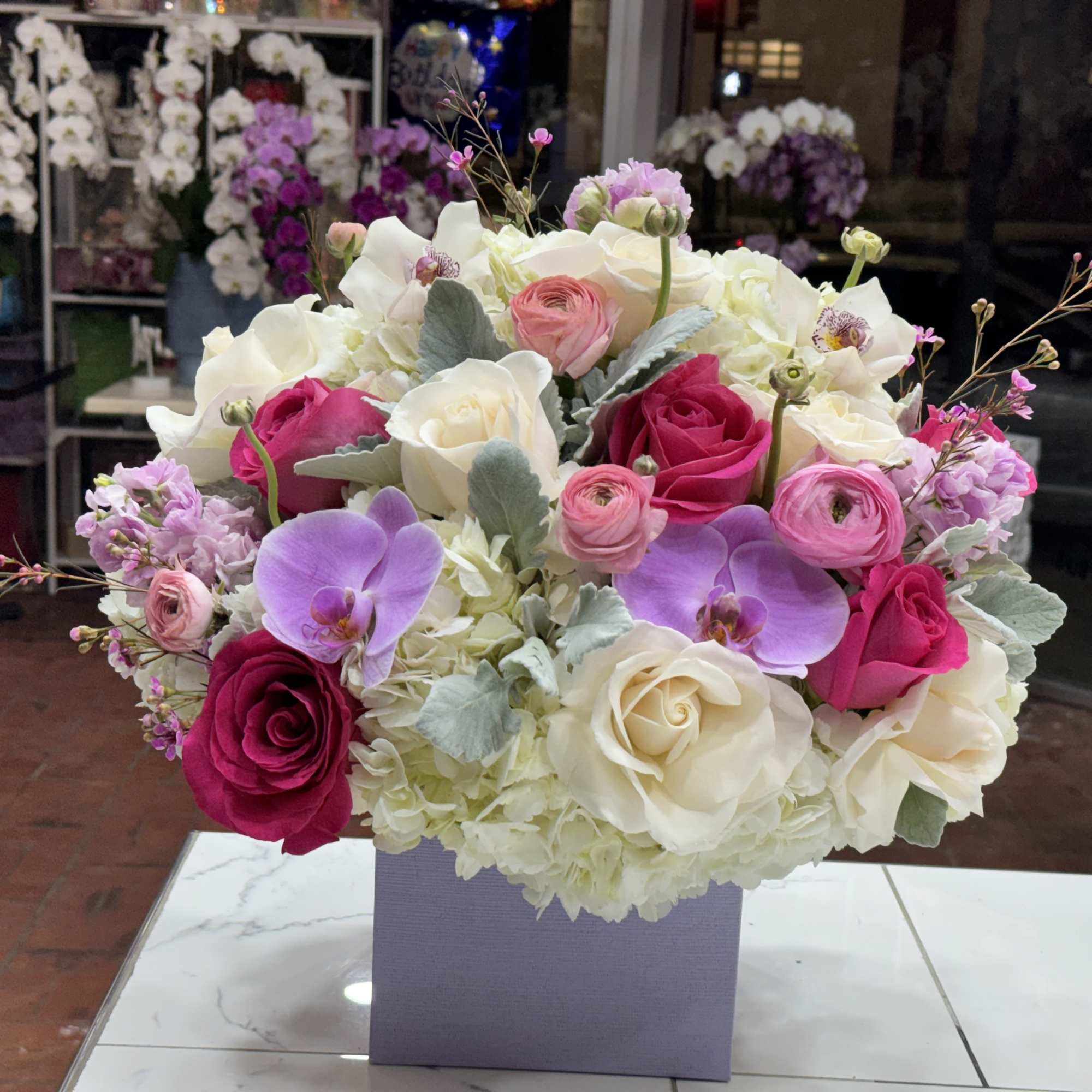 Mixed bouquet of roses, orchids, and hydrangeas in a lavender box