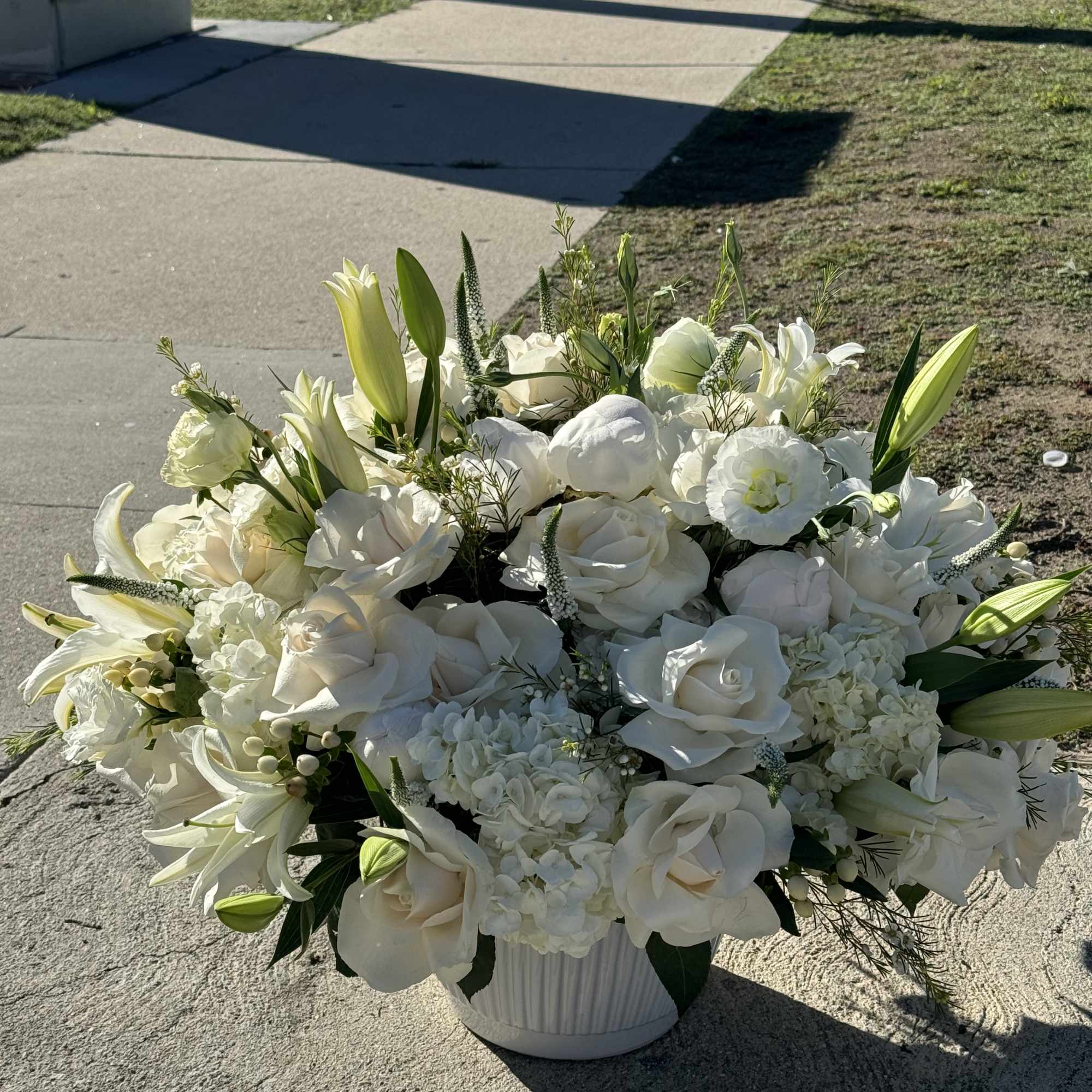 White floral arrangement in a white vase with lilies and roses