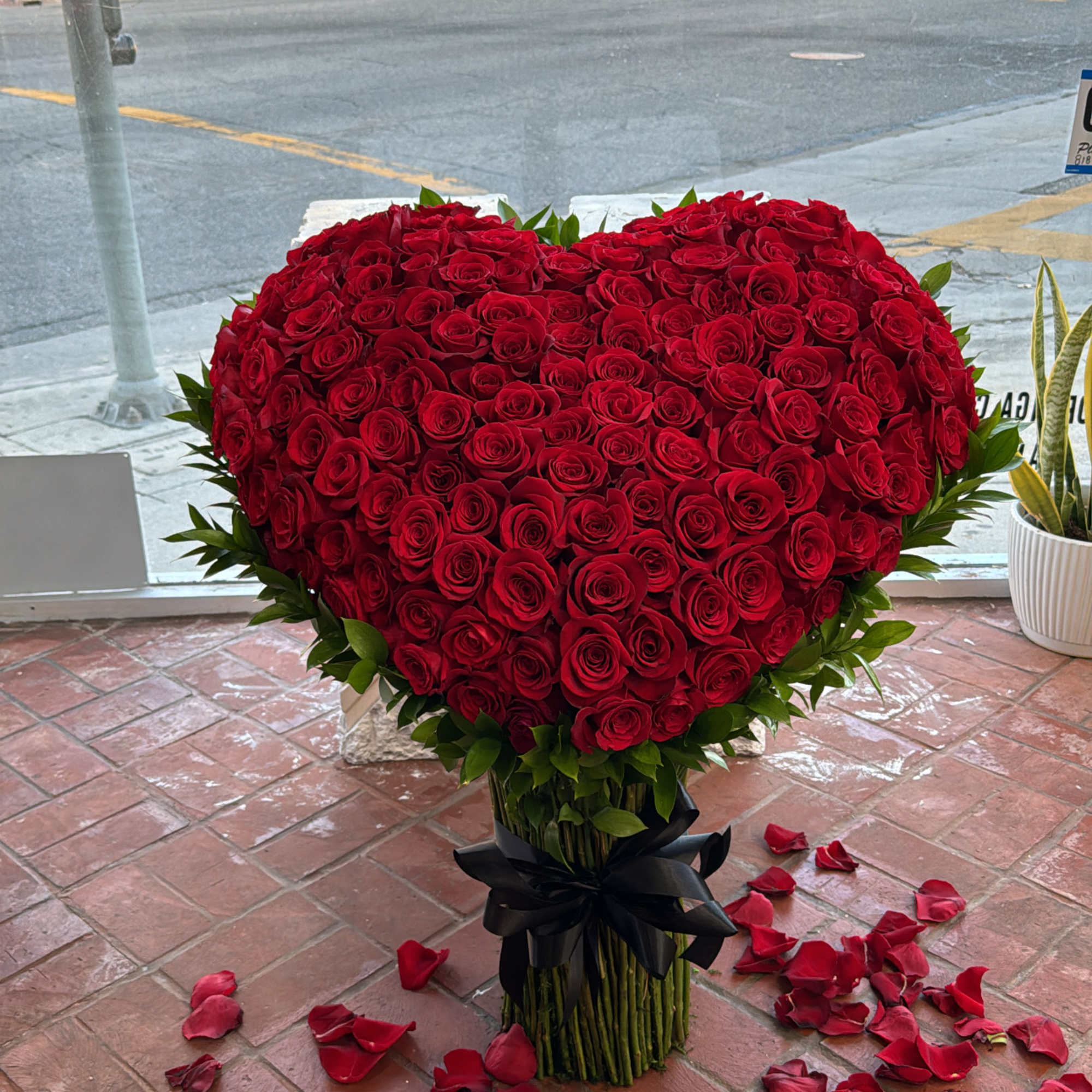 Heart-shaped arrangement of red roses with rose petals on the floor