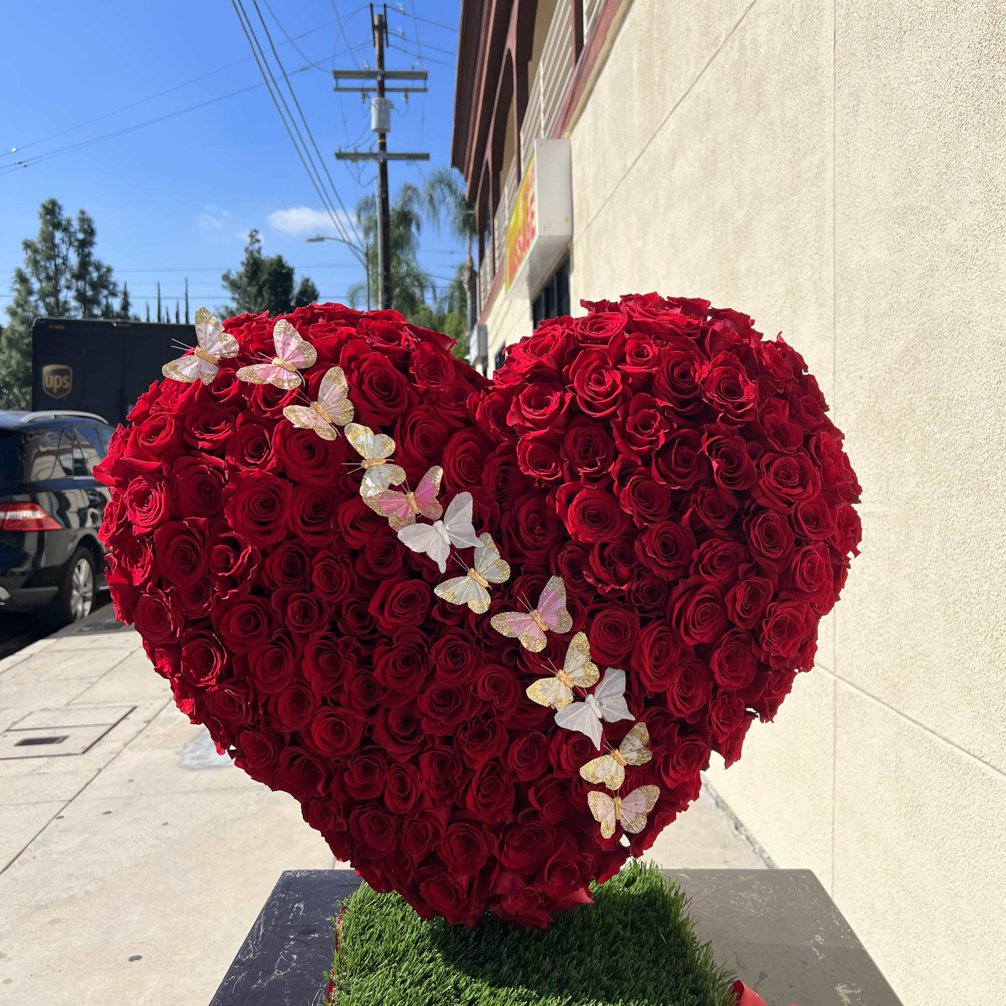 Heart-shaped arrangement of red roses with butterfly decorations on a green base