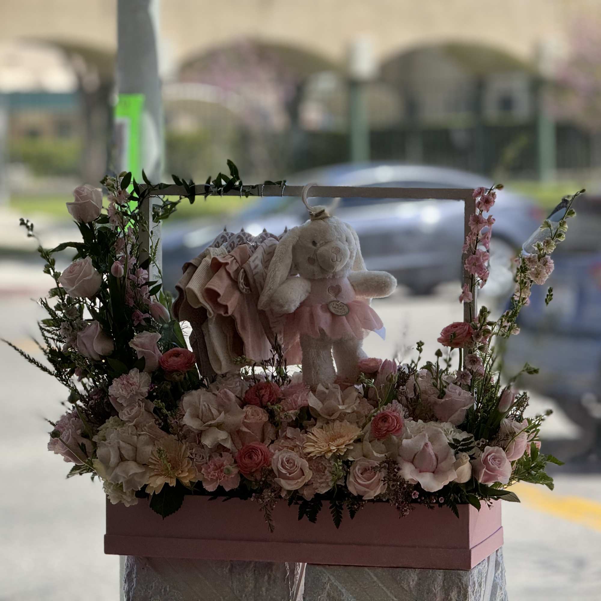 Pink floral basket with a stuffed bunny and folded baby clothes