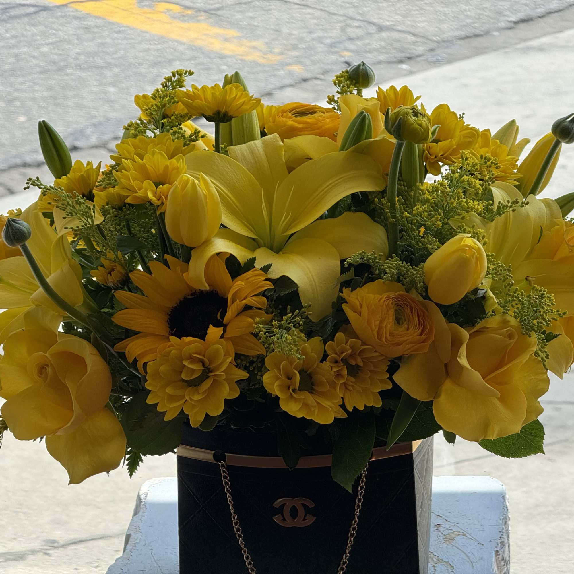 Yellow floral arrangement in a black handbag-style container