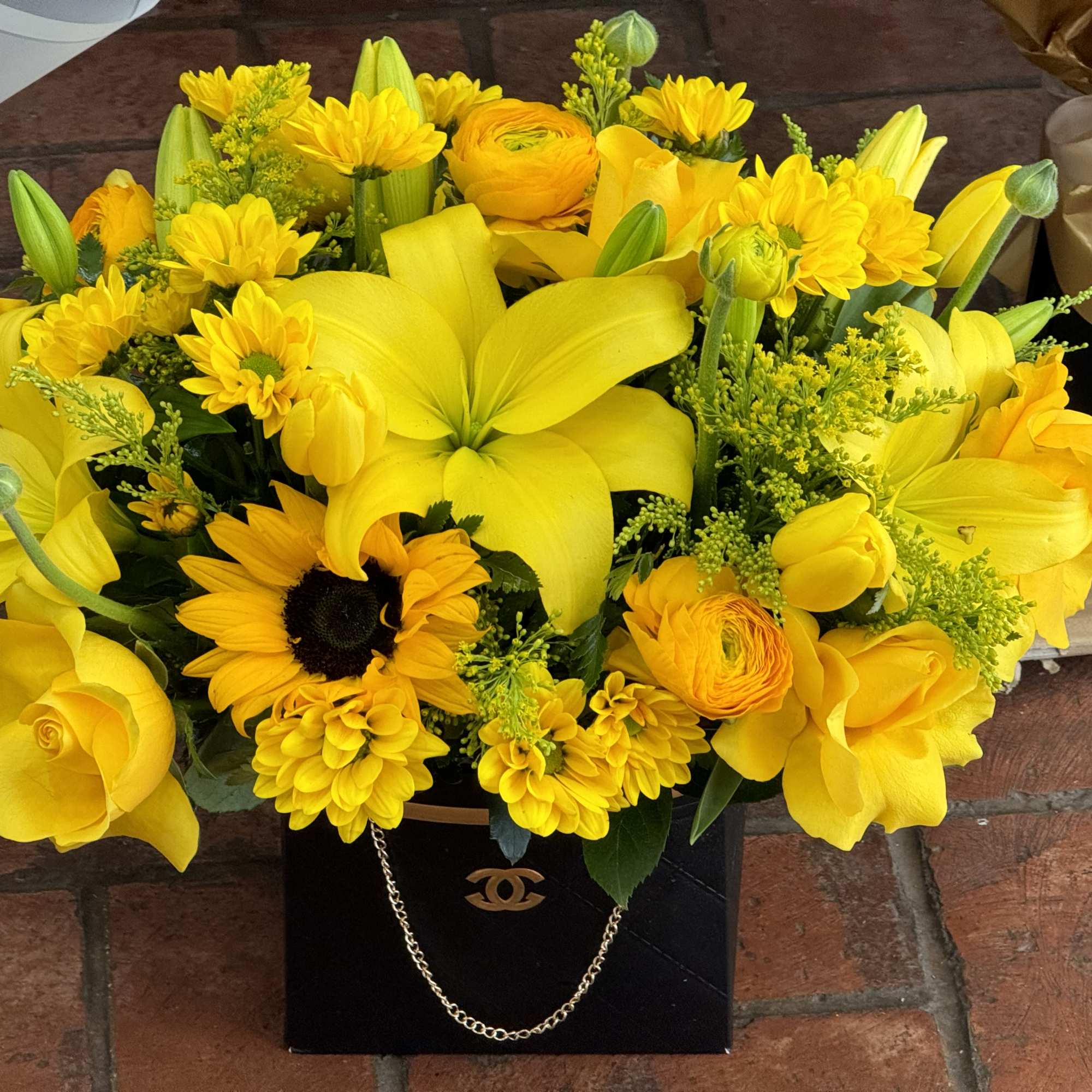 Yellow bouquet with lilies, roses, sunflowers, and daisies in a black gift bag