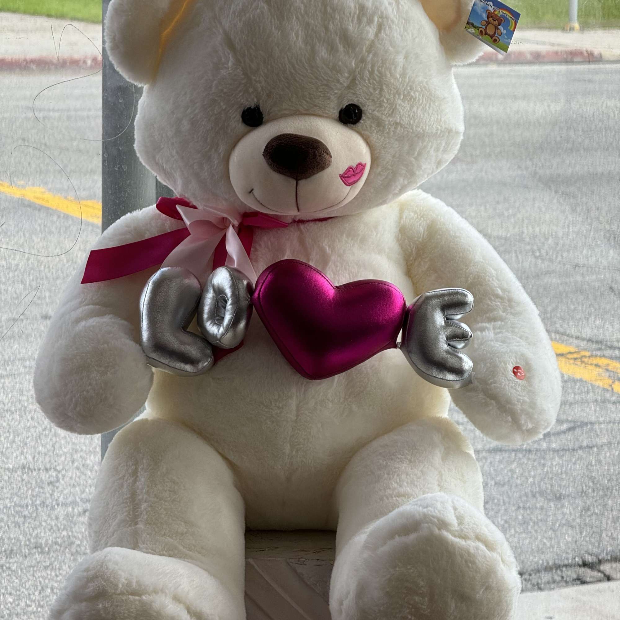 White teddy bear holding a pink heart with "LOVE" letters