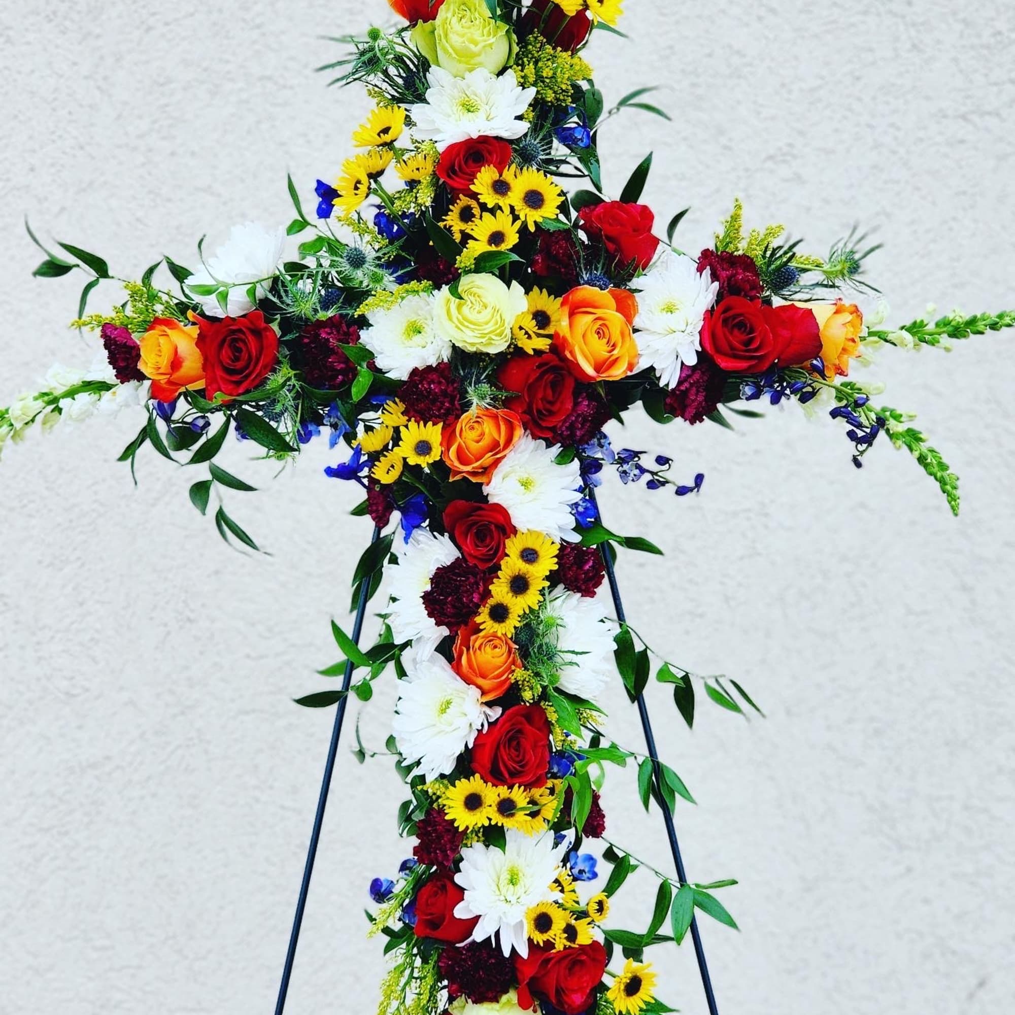 Cross-shaped floral tribute with red, orange, yellow, and white flowers