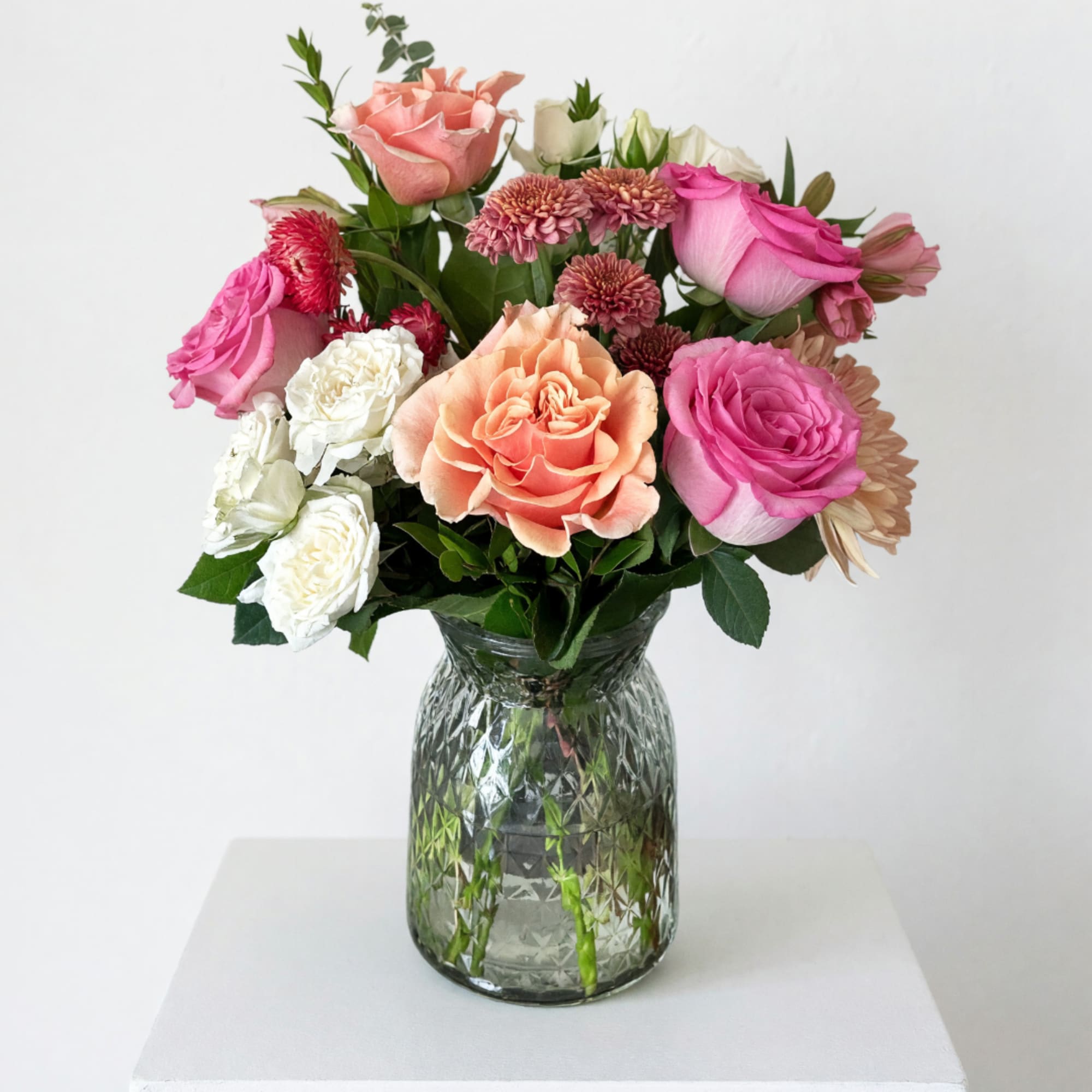 Mixed pink, peach, and white flowers arranged in a glass vase
