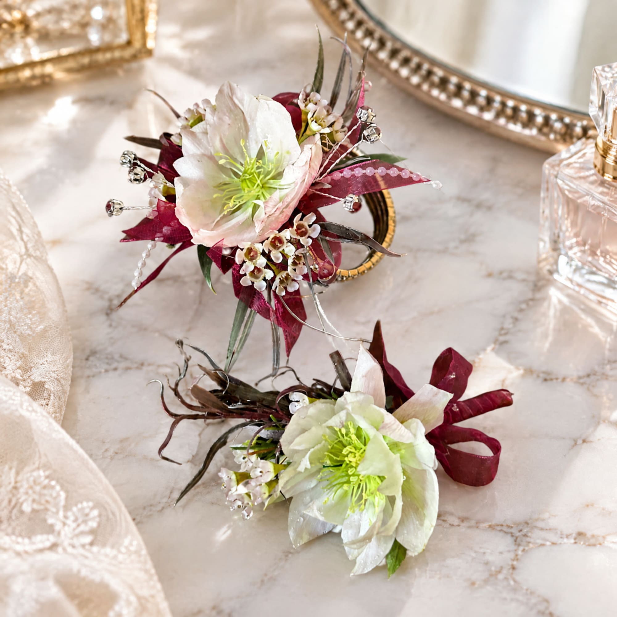 Two floral corsages with white blooms and burgundy accents on a marble surface