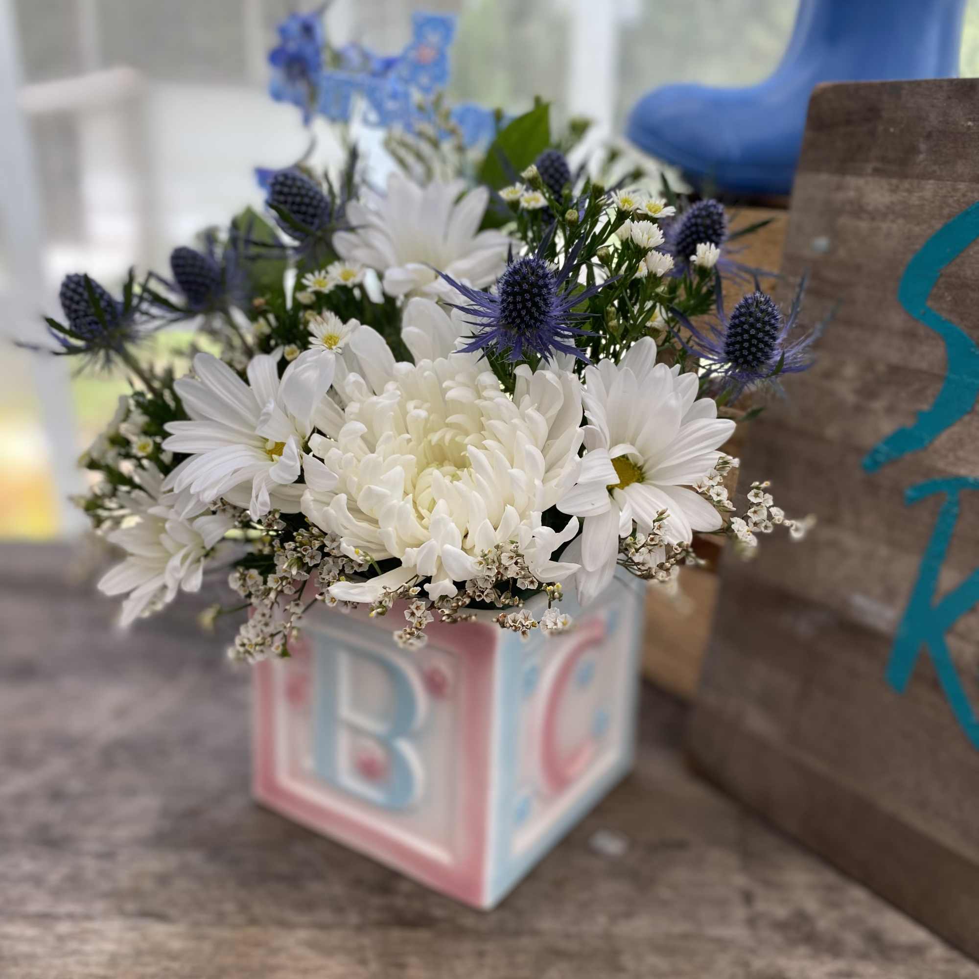 White daisies and mums with blue accents arranged in a pastel baby block cube vase.
