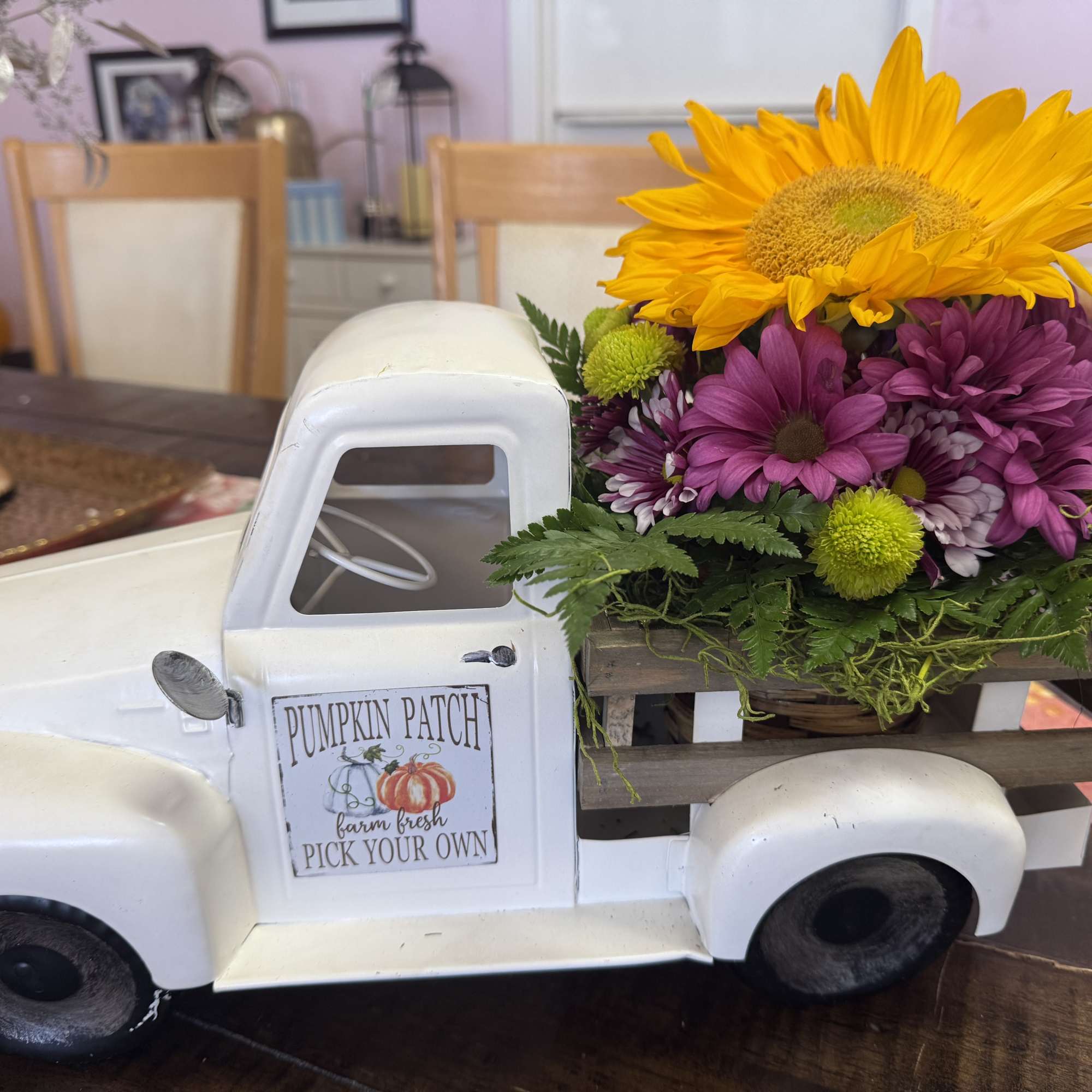 Flower arrangement in a white pickup truck planter with a sunflower and purple daisies