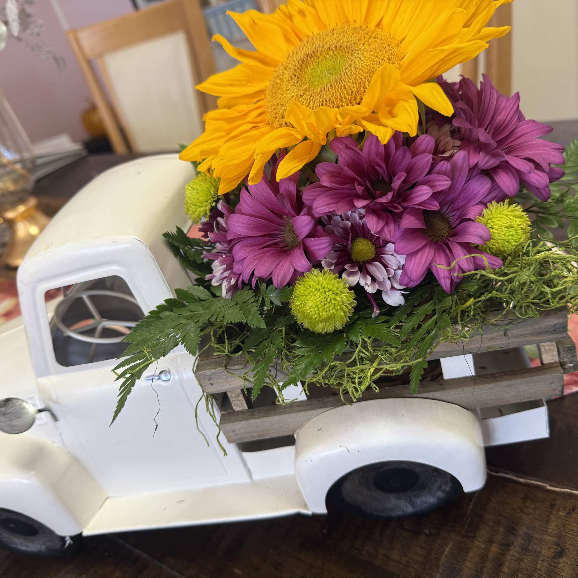 Sunflower and purple daisy arrangement in a white truck-shaped container