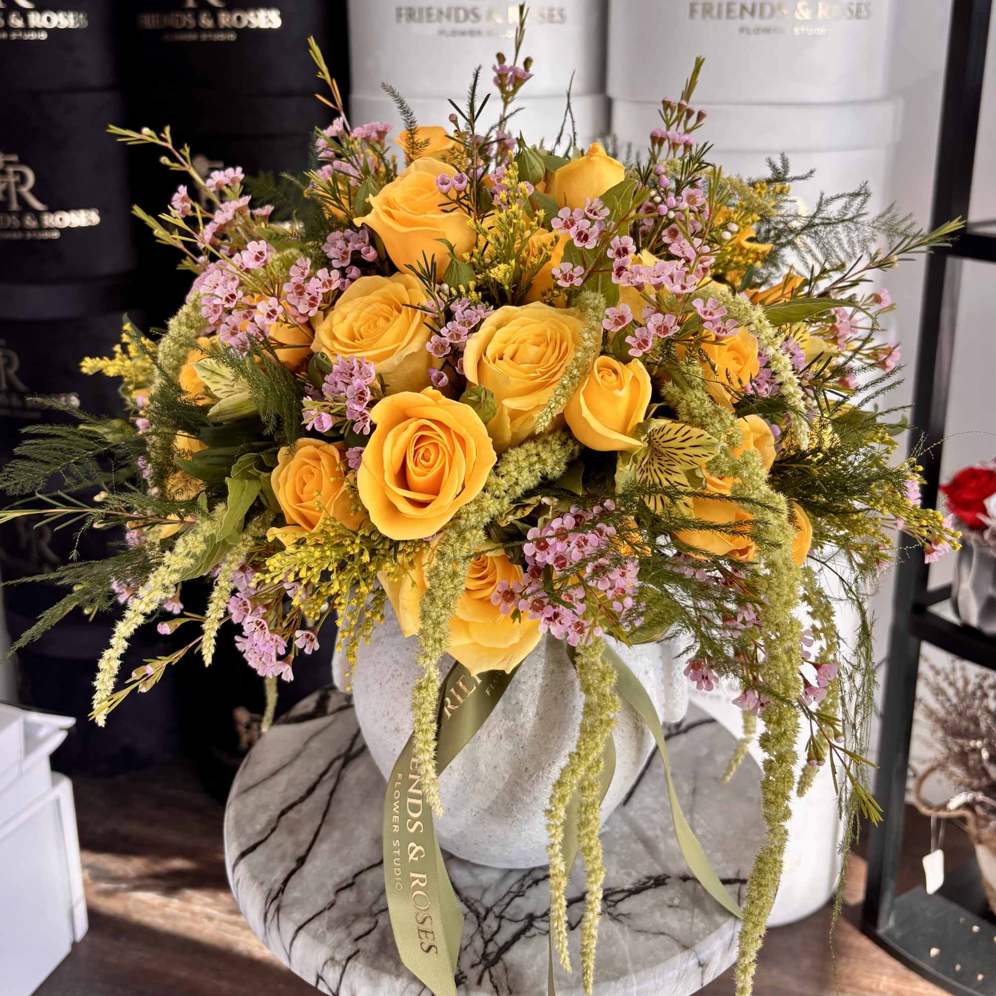 Yellow roses and pink filler flowers arranged in a round vase.