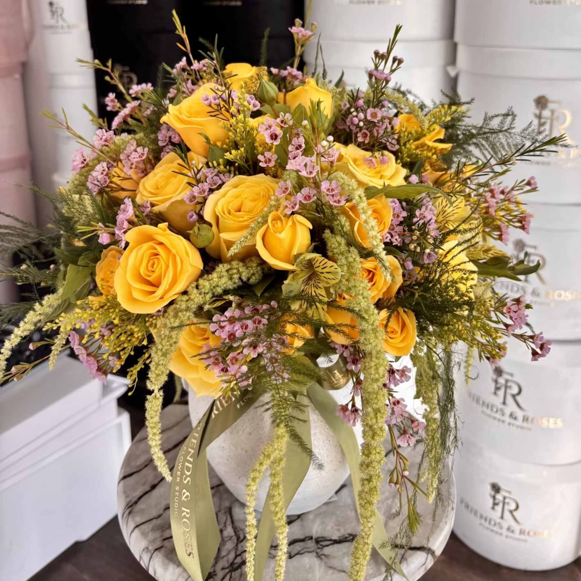 Yellow roses with pink filler flowers in a round vase