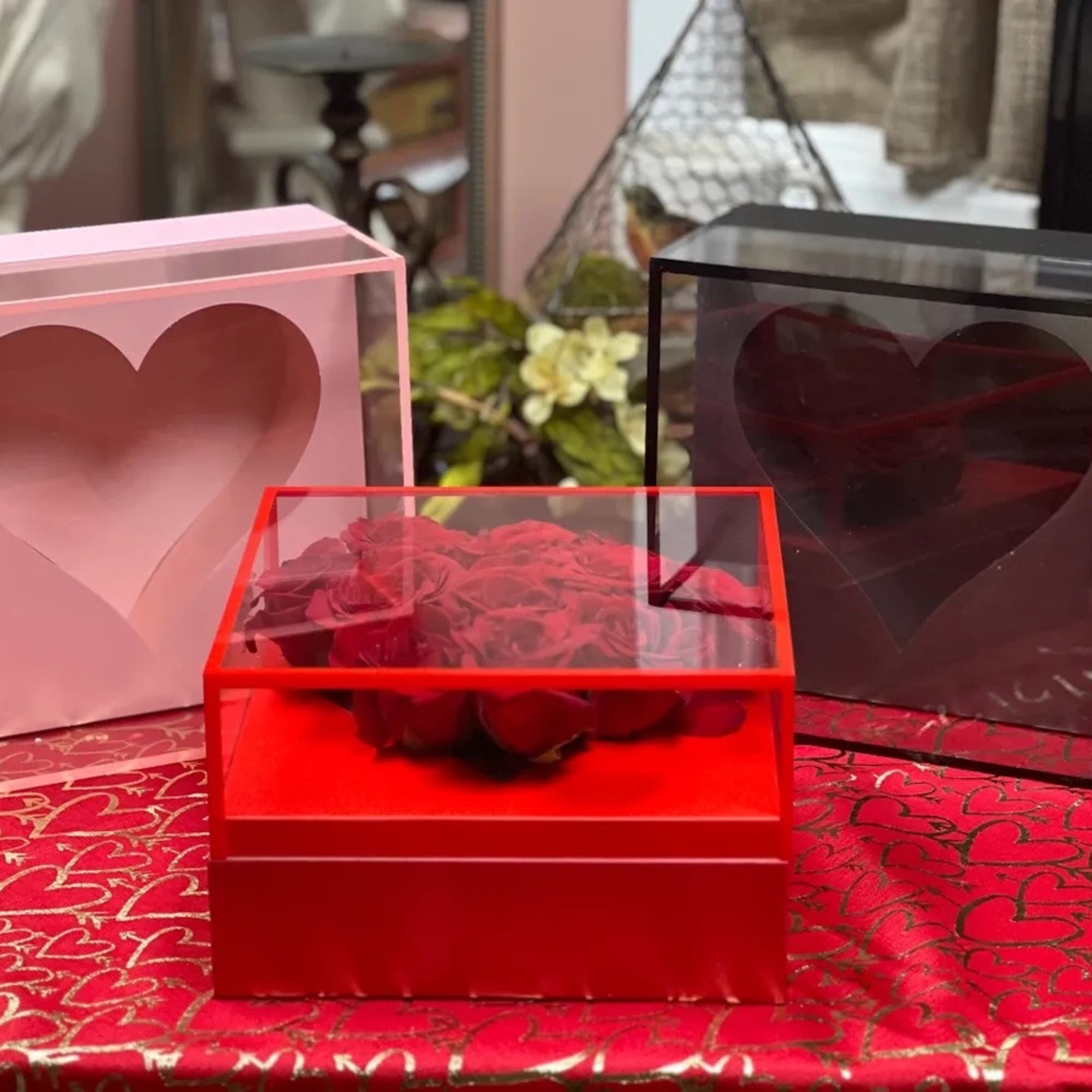 Red roses in a clear heart-shaped box with pink and black heart boxes nearby