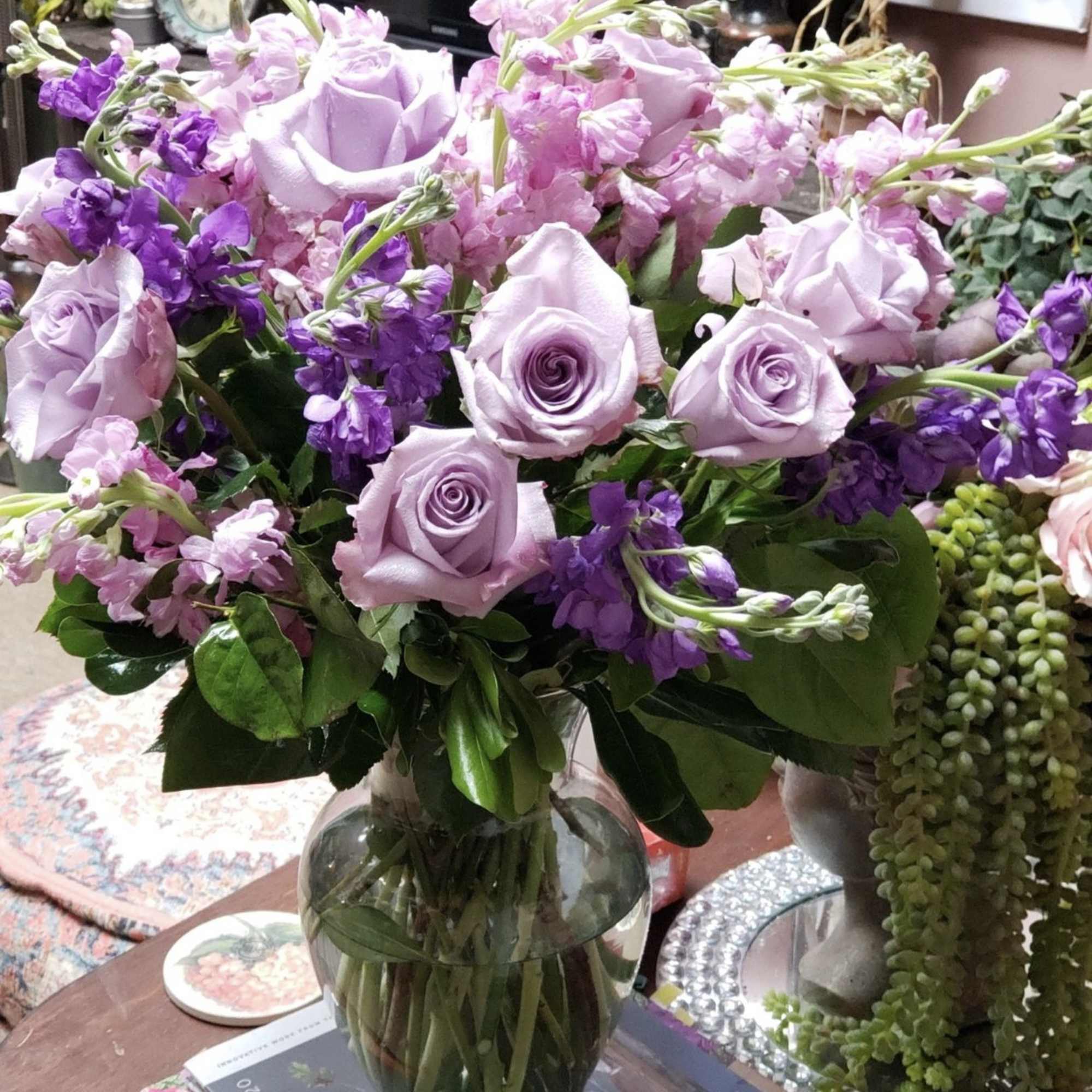 Lavender roses and purple flowers arranged in a clear glass vase