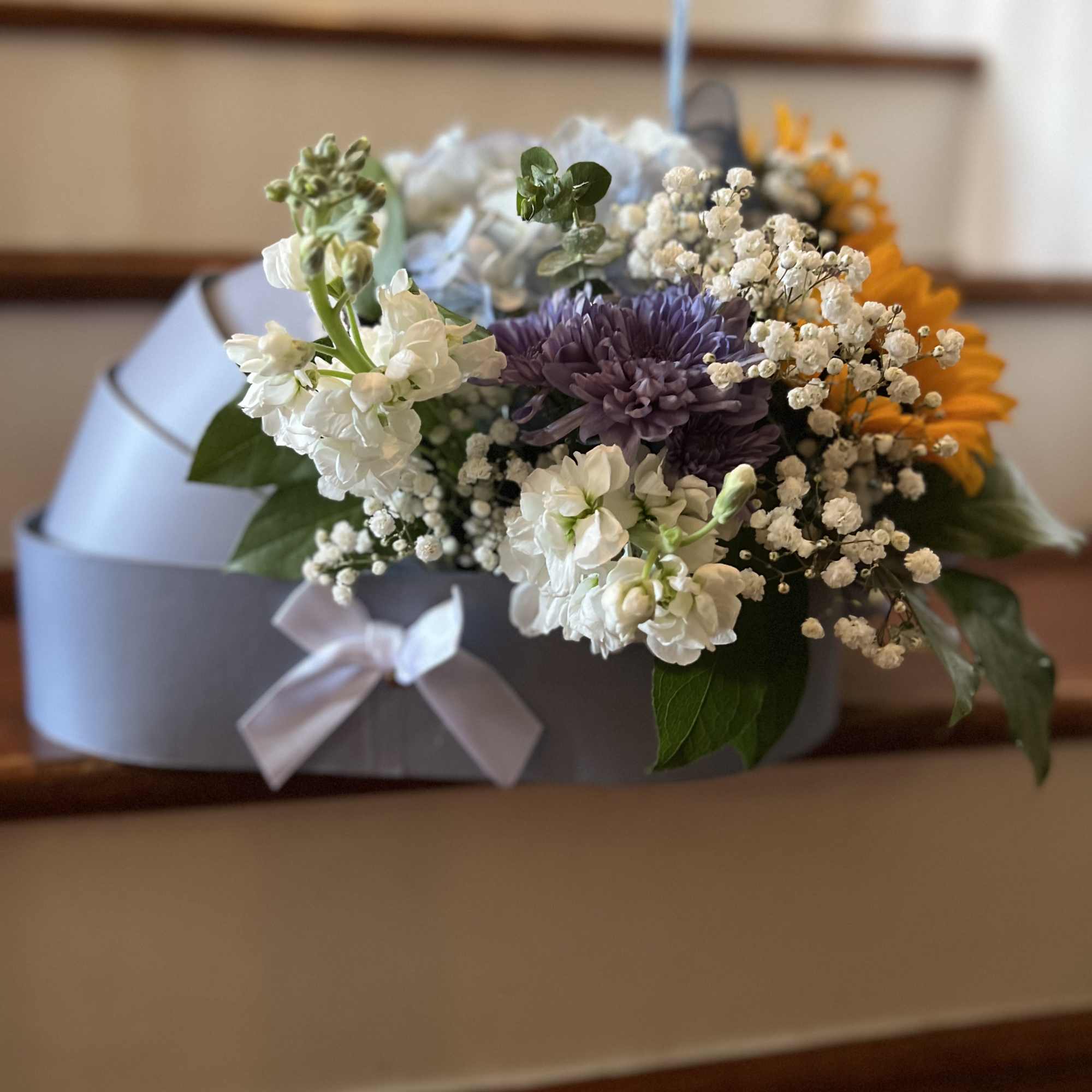 Flower arrangement in a gray box with purple, white, and orange blooms