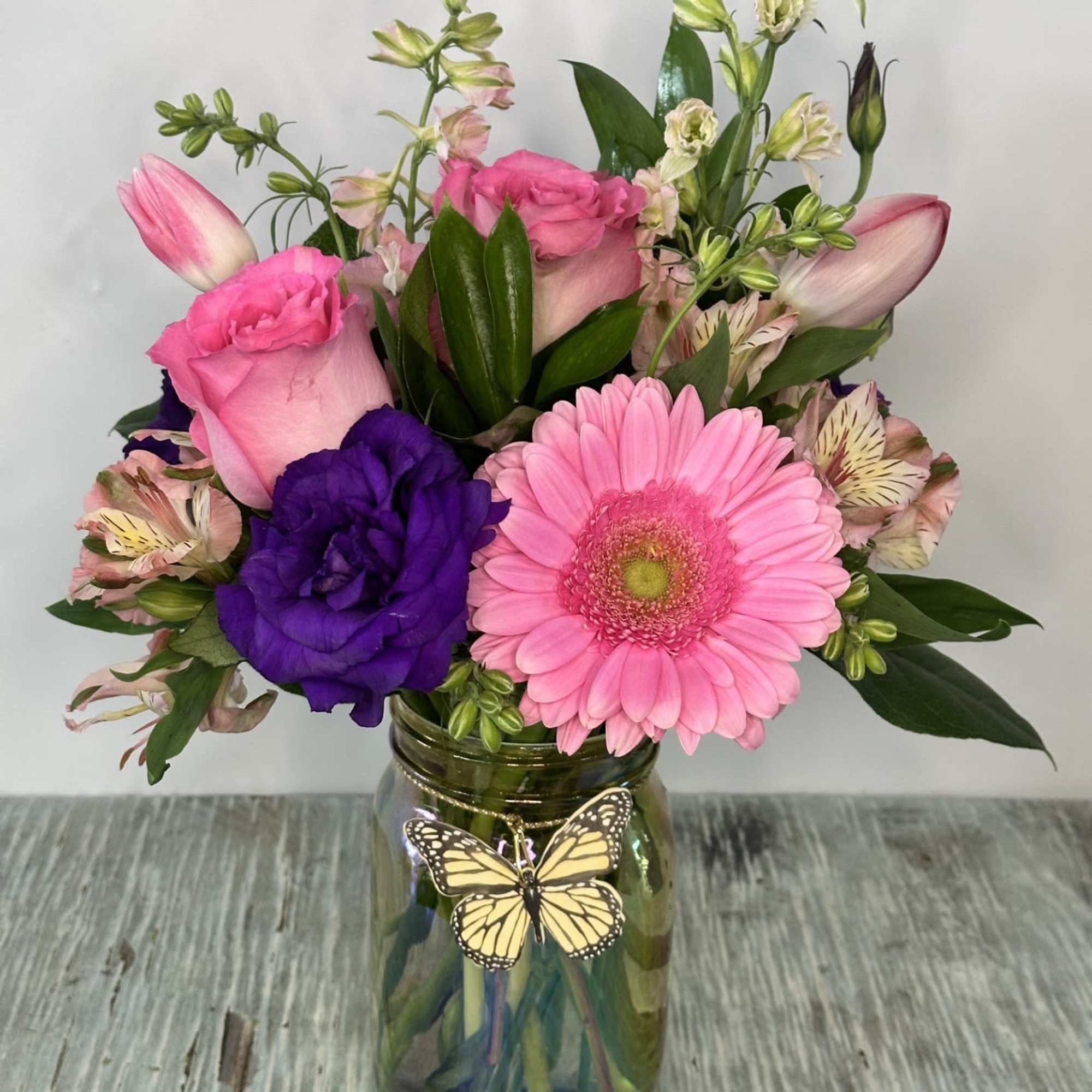 Pink and purple mixed bouquet in a glass jar with a butterfly decoration