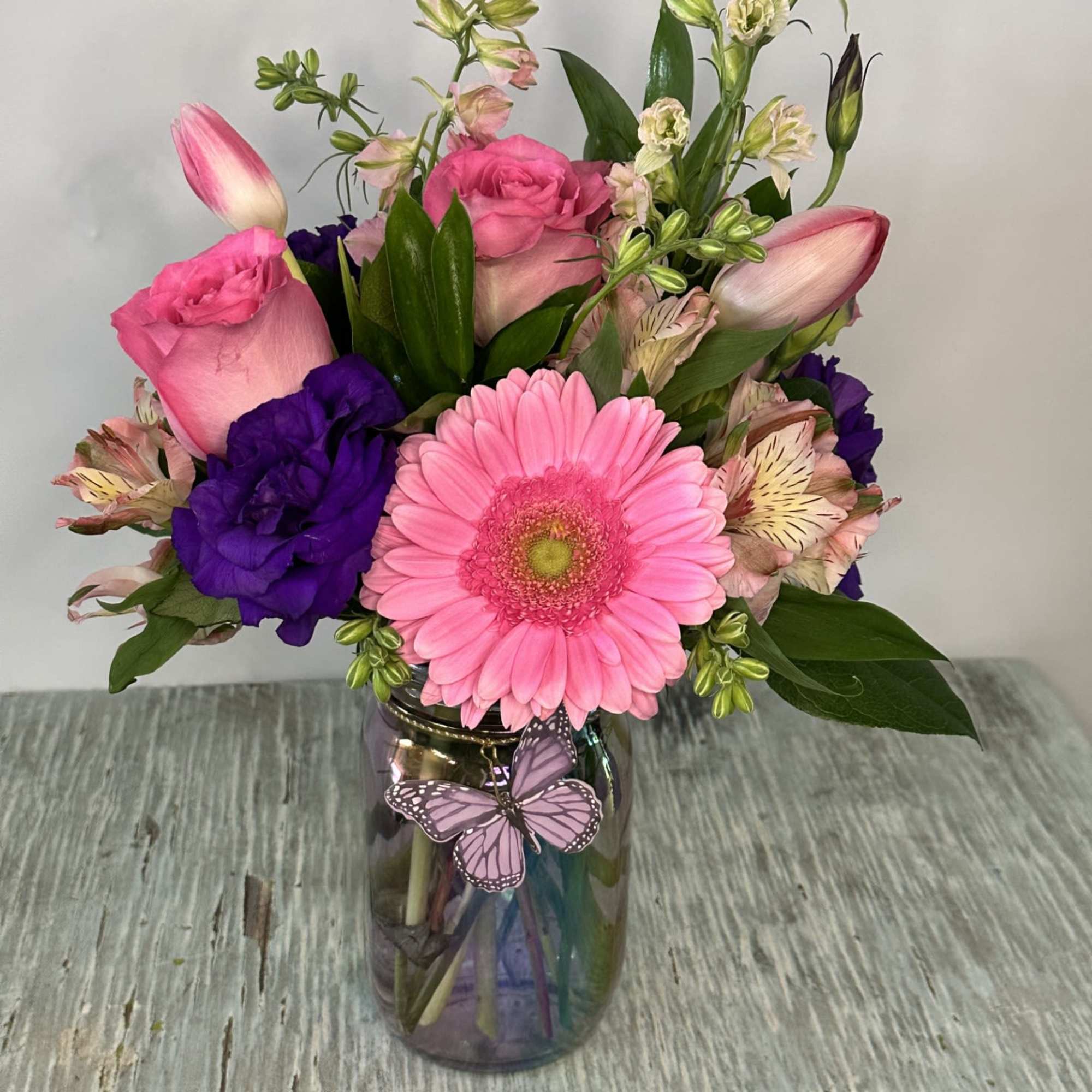 Pink and purple mixed bouquet in a glass vase with a butterfly decoration