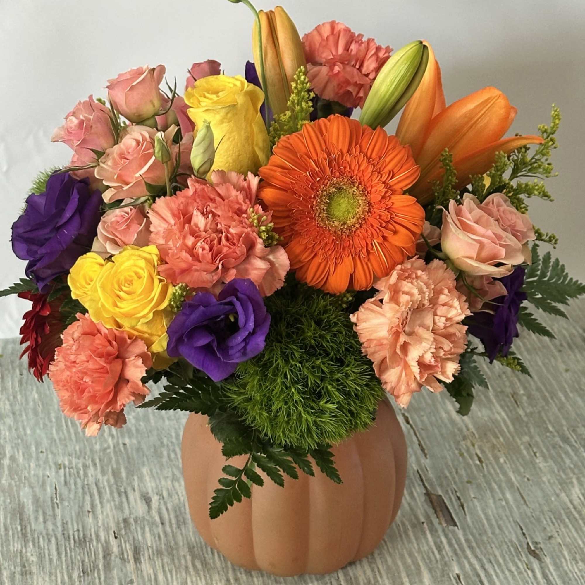 Mixed bouquet in a pumpkin-shaped vase with orange, pink, purple, and yellow flowers
